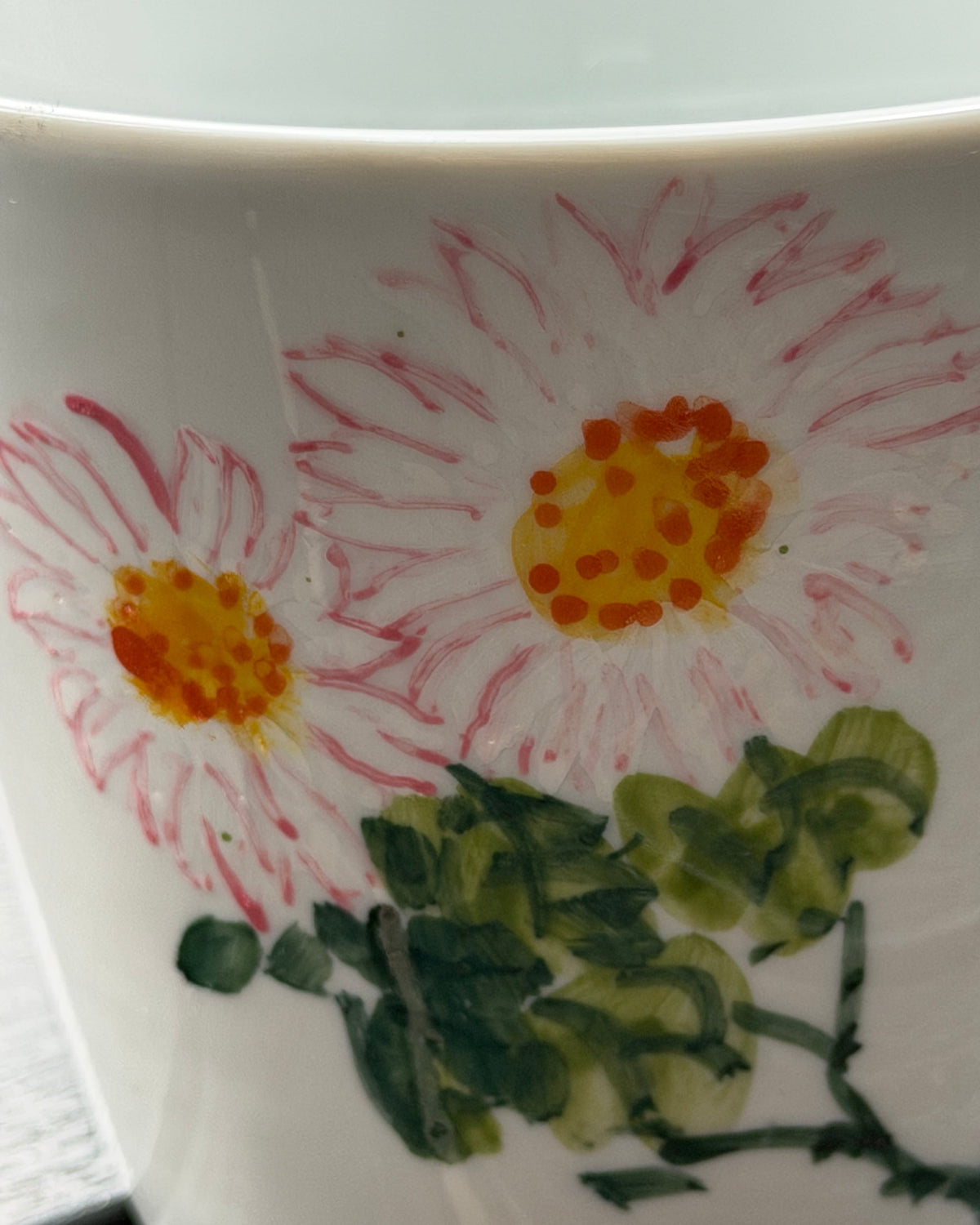 Macro detail of hand-painted daisy brushwork on Blushing Daisy ceramic mug – pink petals and orange center in underglaze