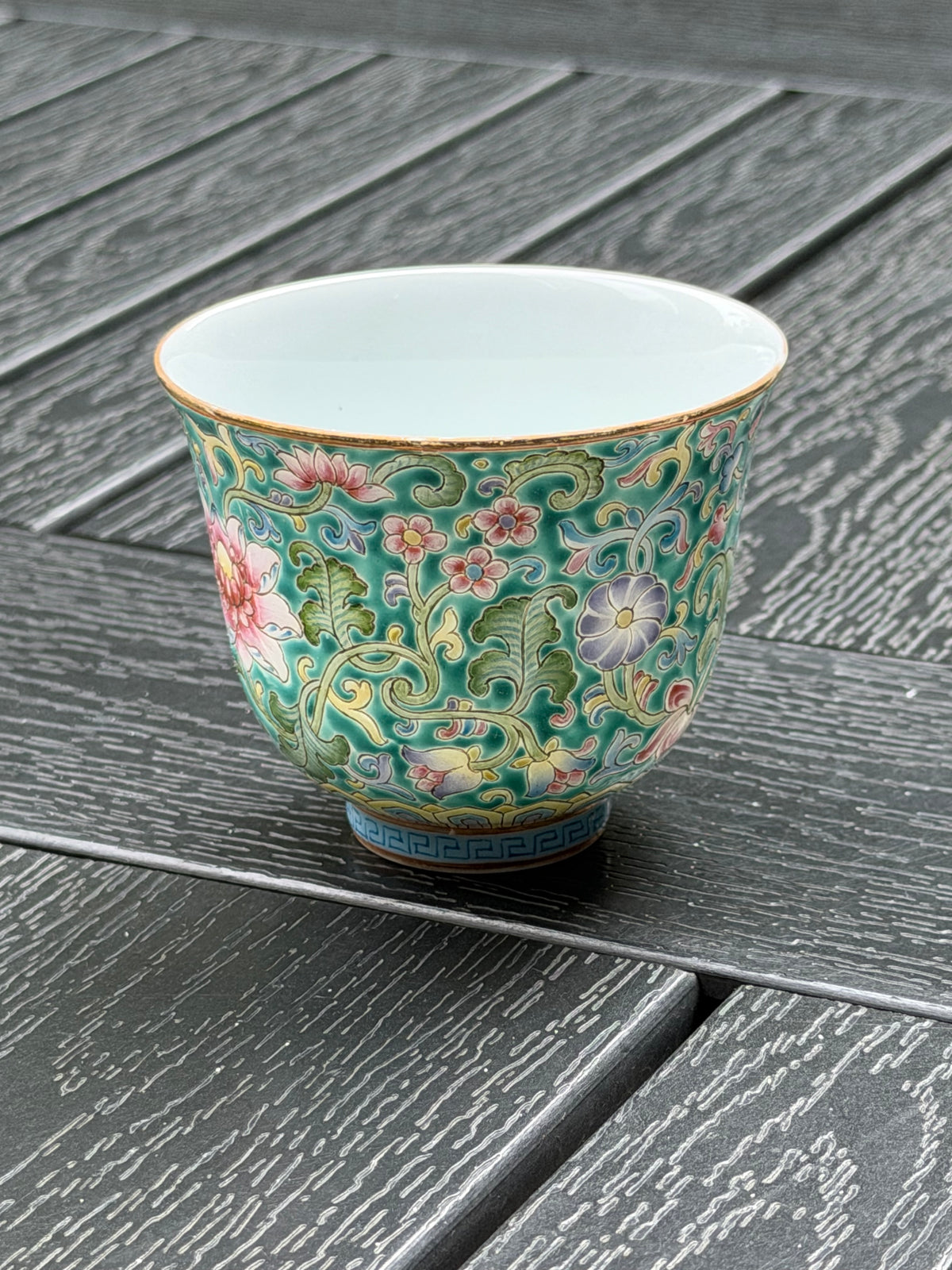 Three-quarter view of the enamel-painted teacup showing its shape, floral design and white interior
