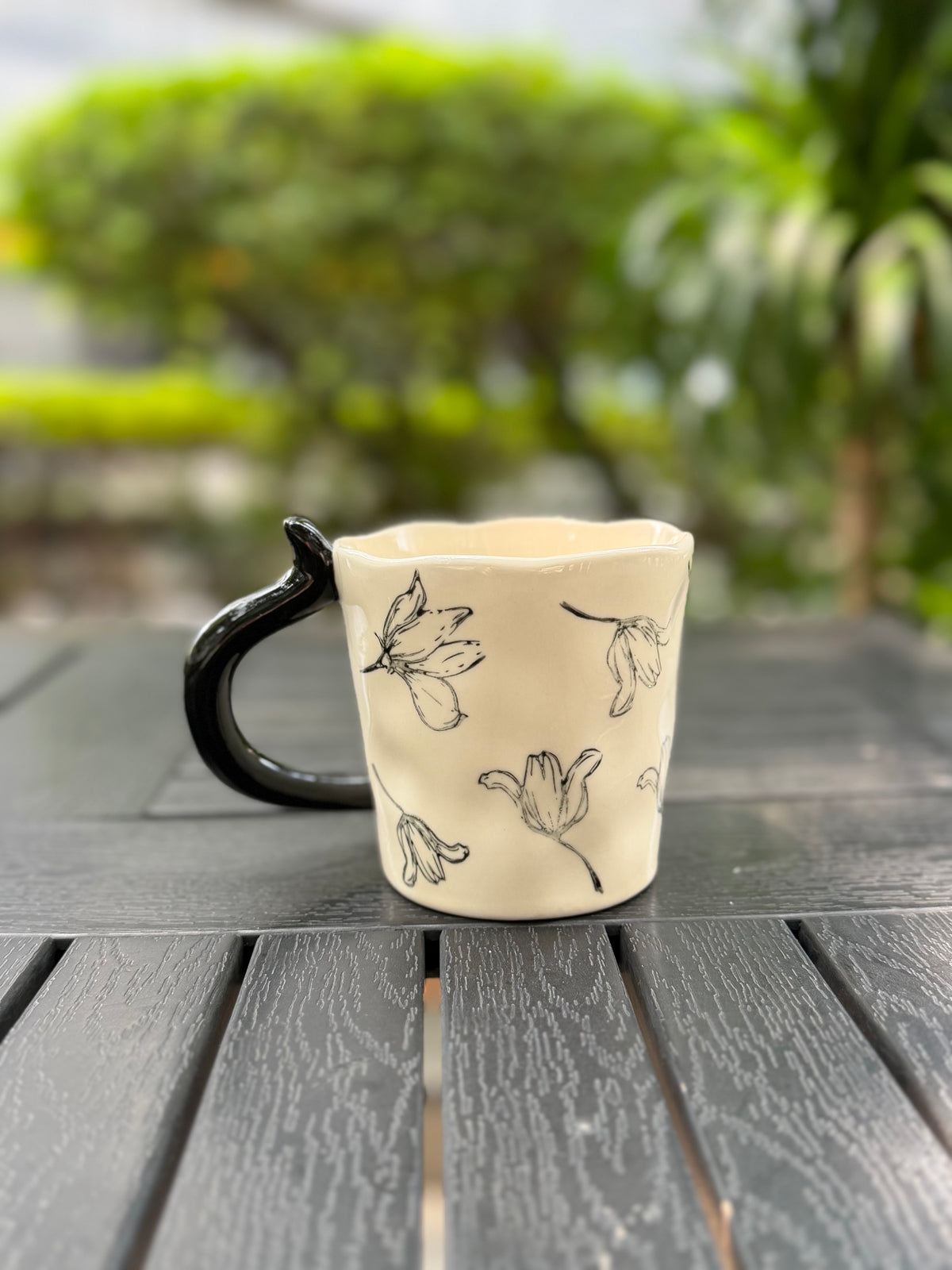 Reverse side of the floral ceramic mug photographed outdoors against softly blurred greenery