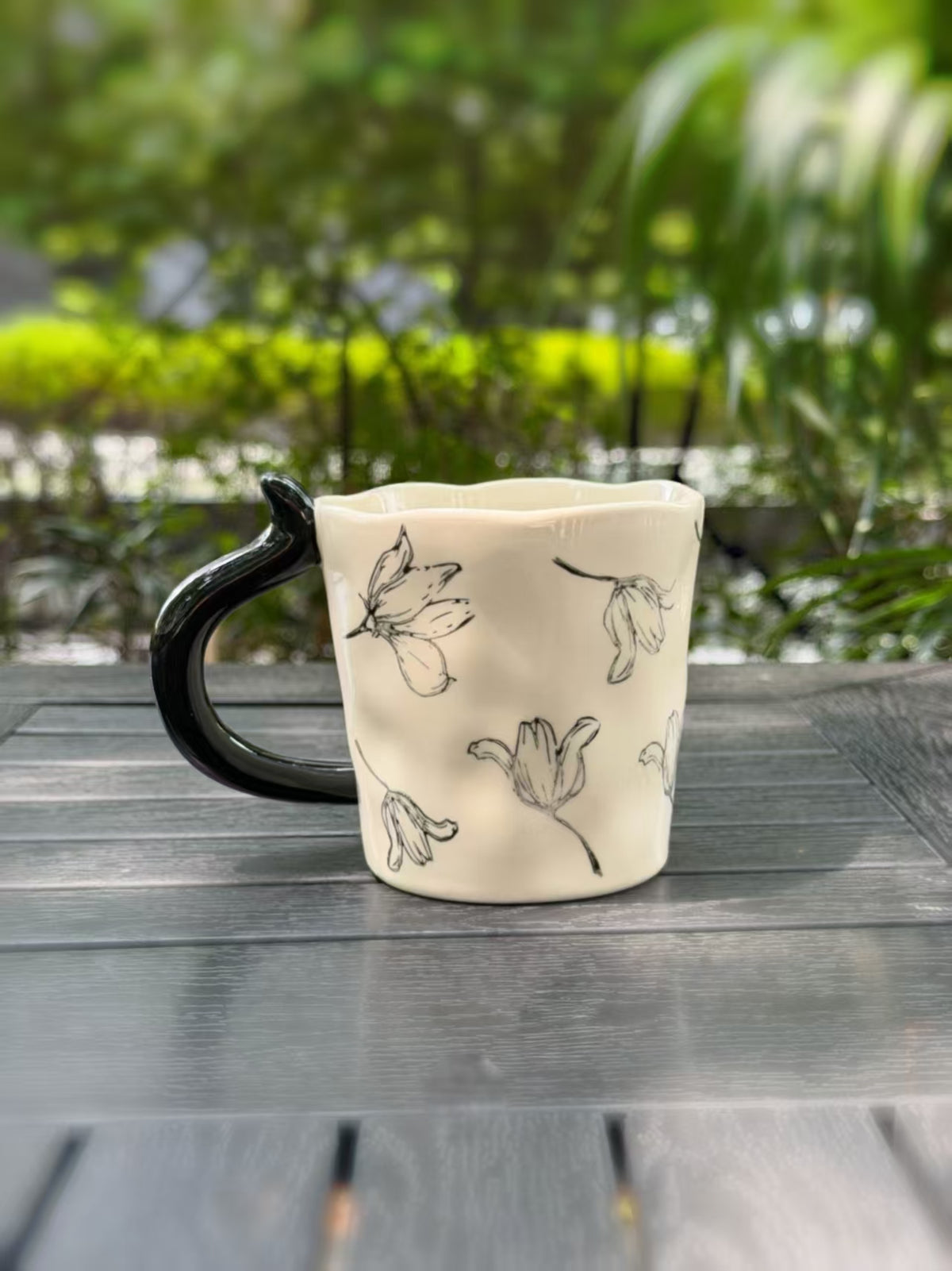 Back view of the cream mug showing delicate floral outlines and the black handle