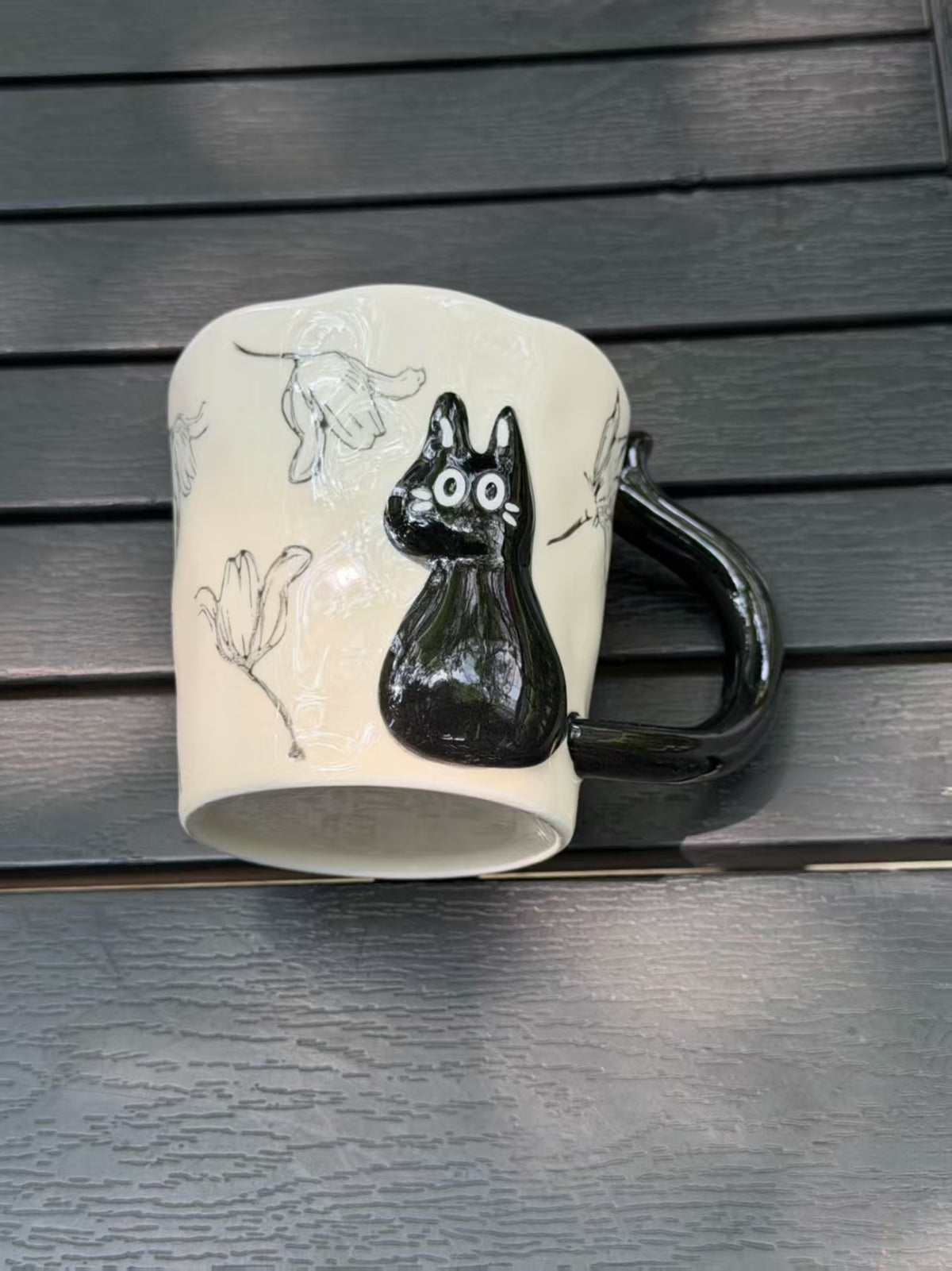 Mug resting on its side, showing the raised black cat, floral outlines and ceramic base