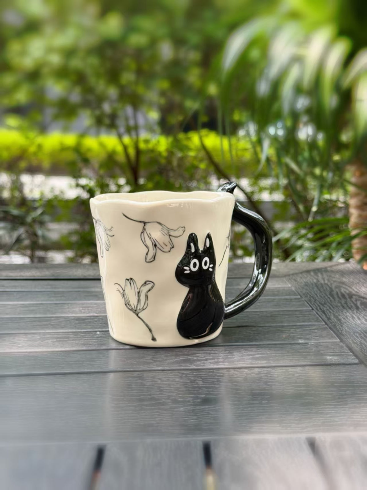 Side view of the ceramic mug showing the black cat relief and floral outlines wrapping around the cup