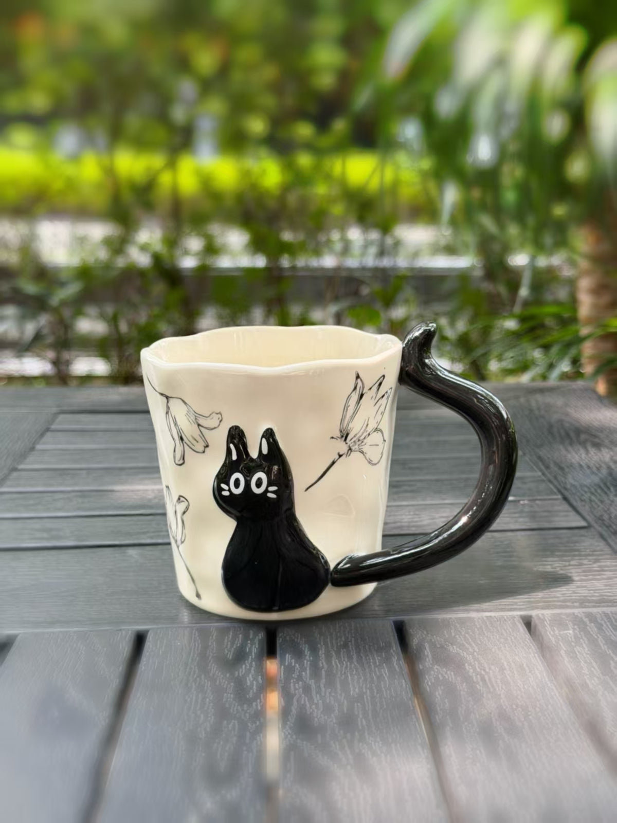 Front view of the cream ceramic mug with a raised black cat, floral outlines and glossy black handle