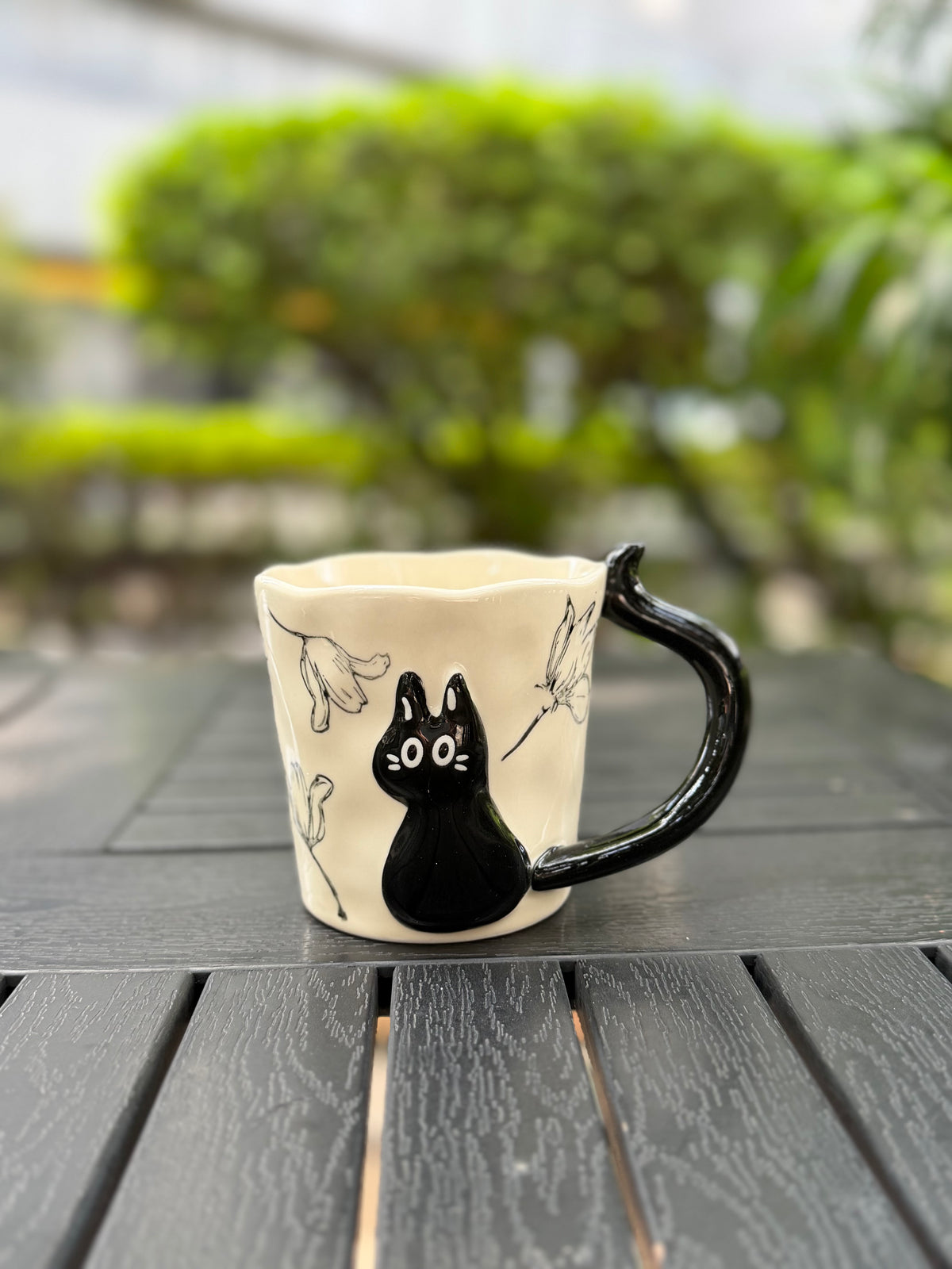 Black cat relief mug on an outdoor table with its floral design and softly blurred garden background