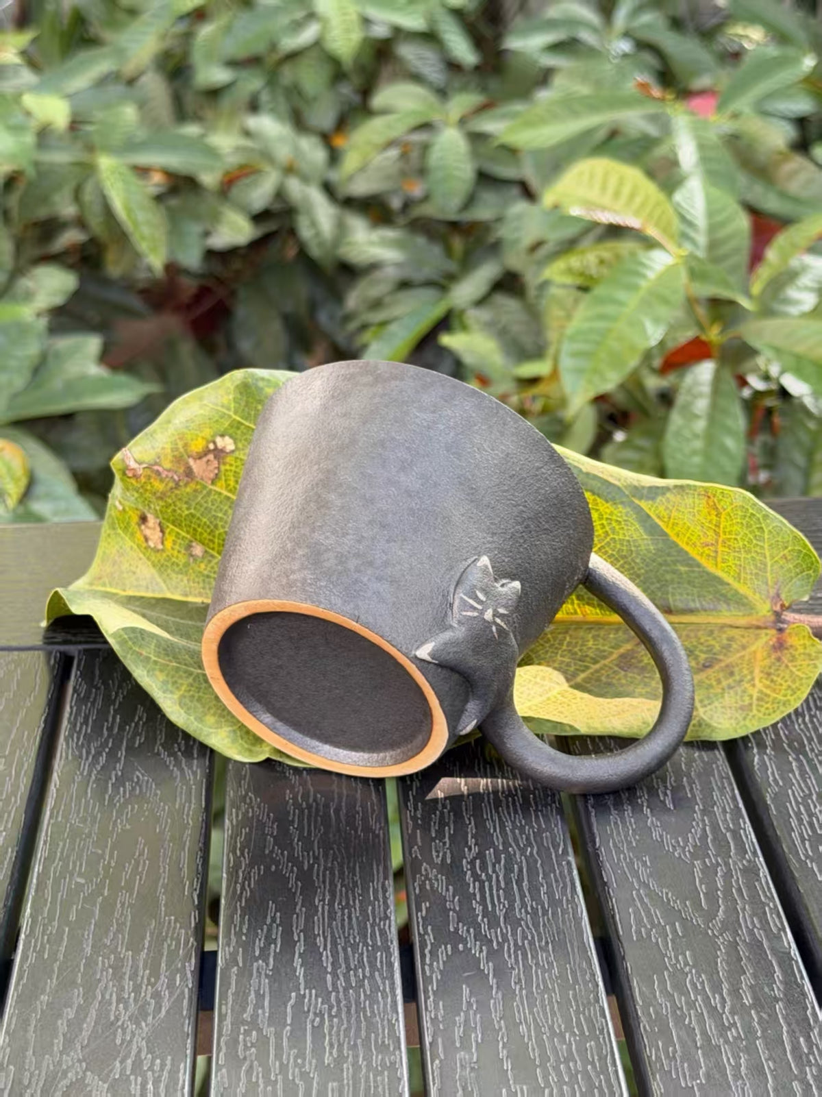 Black cat ceramic cup tilted to show the base and sculptural cat detail