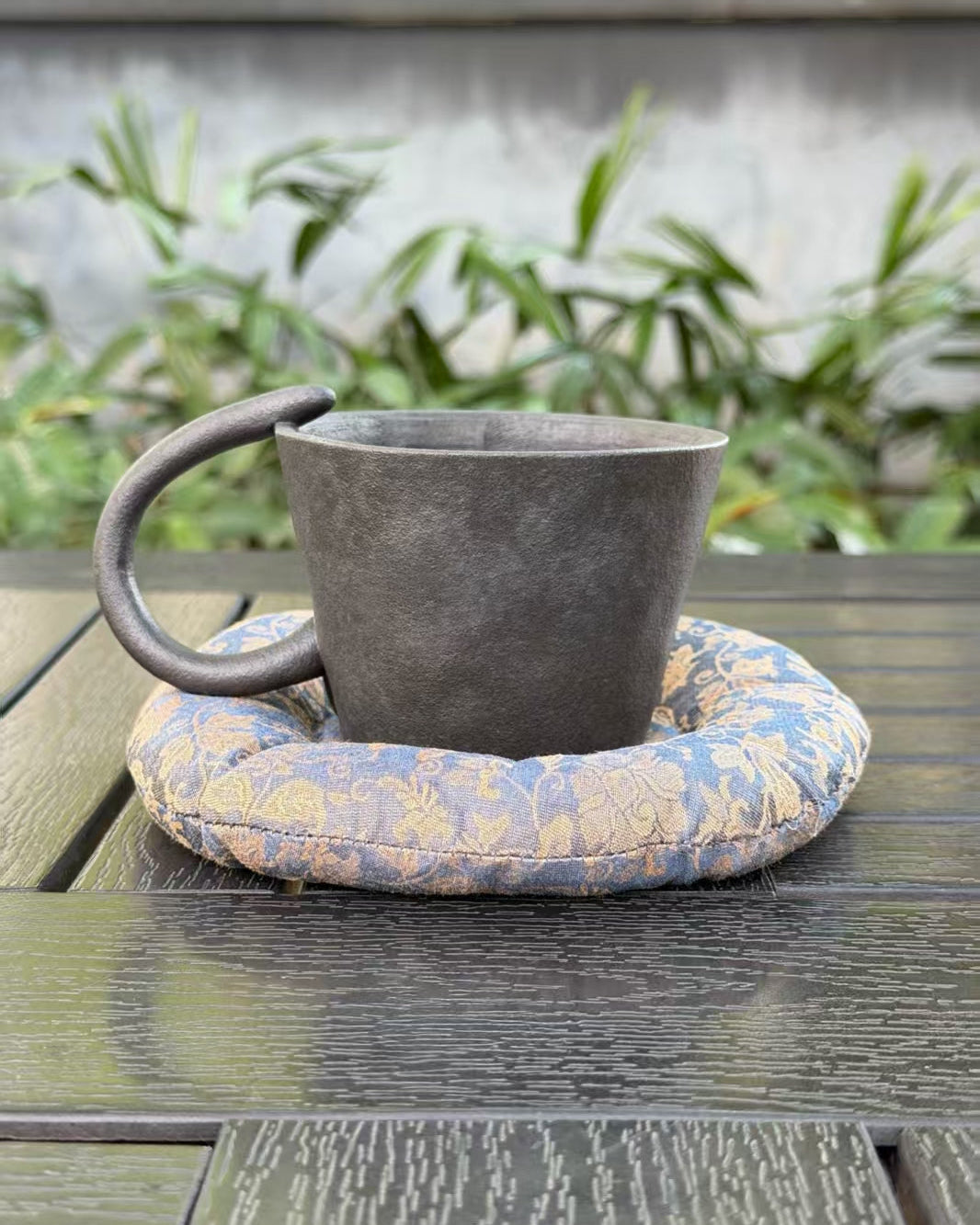 Back view of black cat ceramic cup with curved tail handle and blue and gold patterned cushion