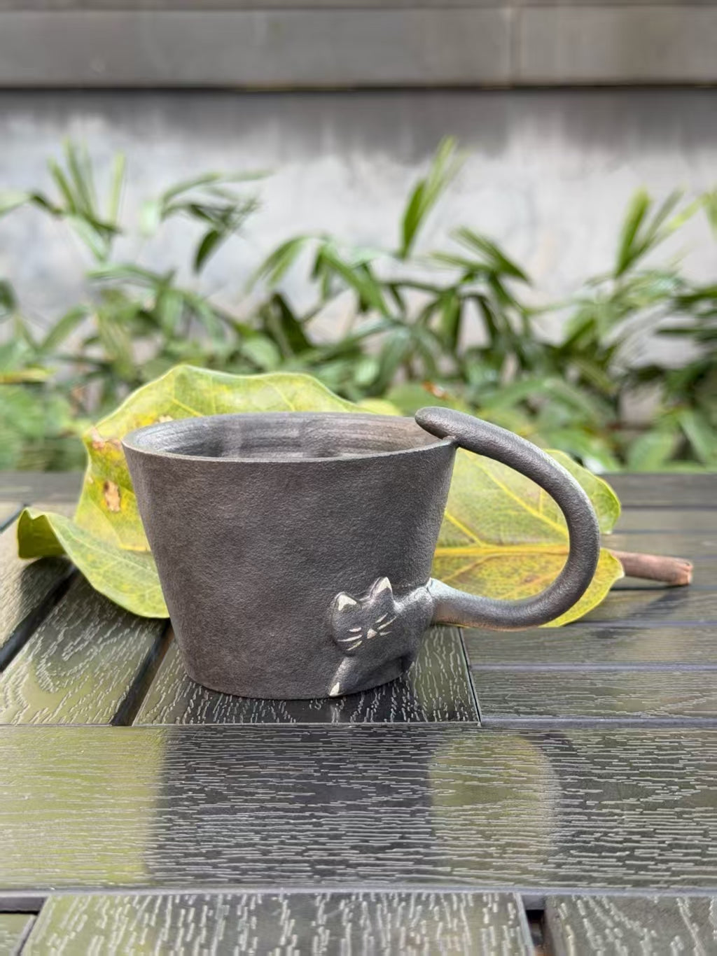 Black ceramic cat cup with textured dark glaze and sculptural tail handle