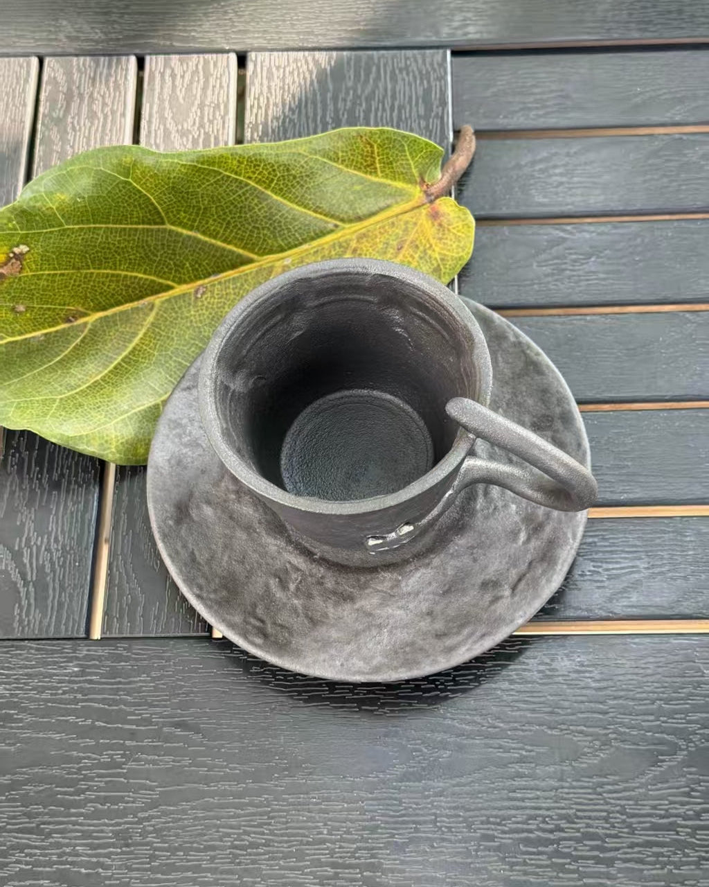 Top view of black ceramic cat cup and matching saucer with textured dark glaze
