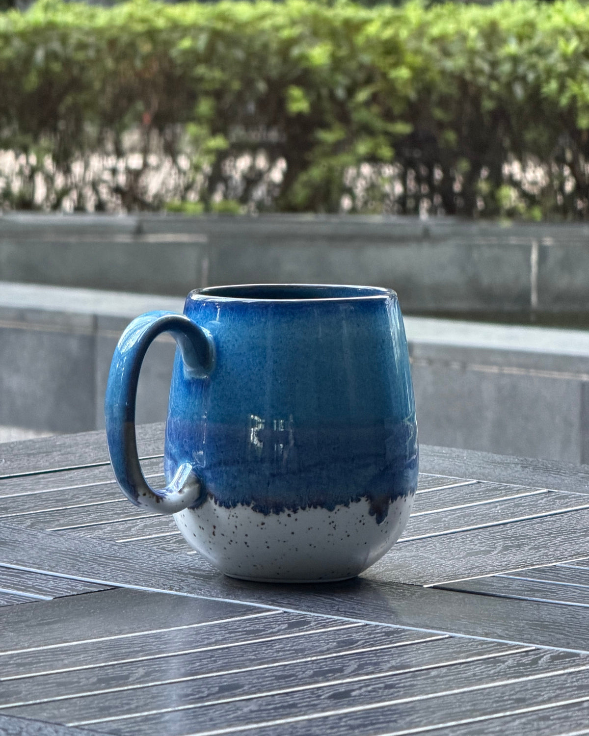 Angled side view of Coastal Tide oversized mug showing ocean blue and violet reactive glaze over a speckled cream base
