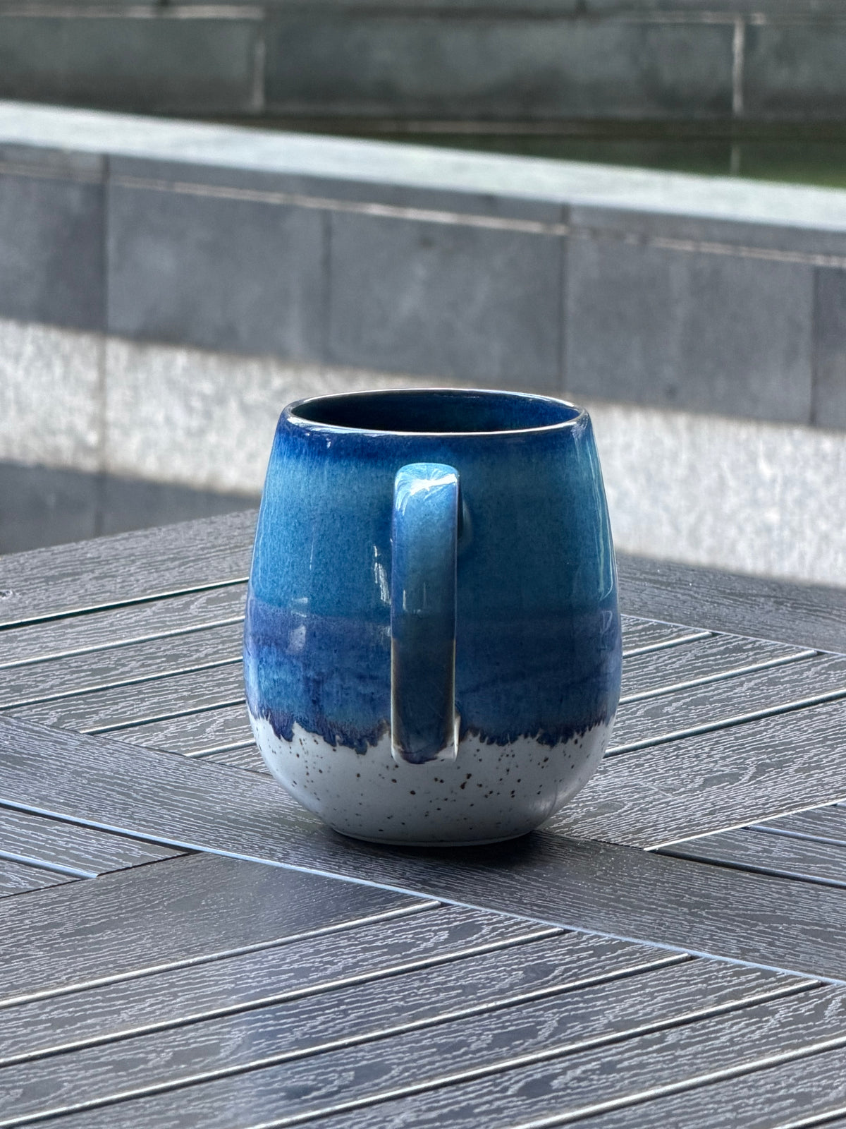 Angled profile of Coastal Tide reactive glaze mug showing its large curved handle and natural blue glaze variation