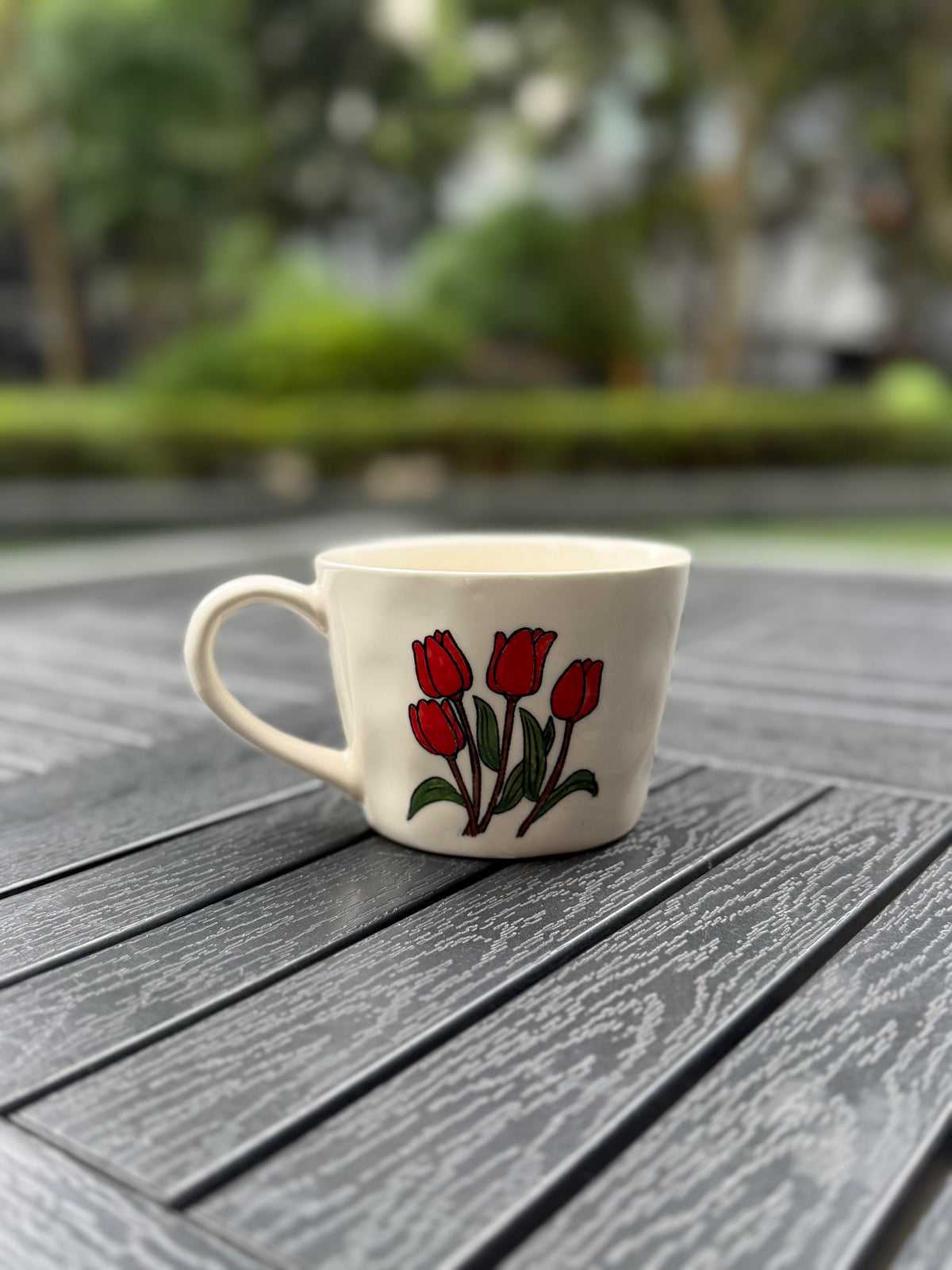 Back-angle view of a warm cream coffee mug with four red tulips, green leaves, and a curved handle