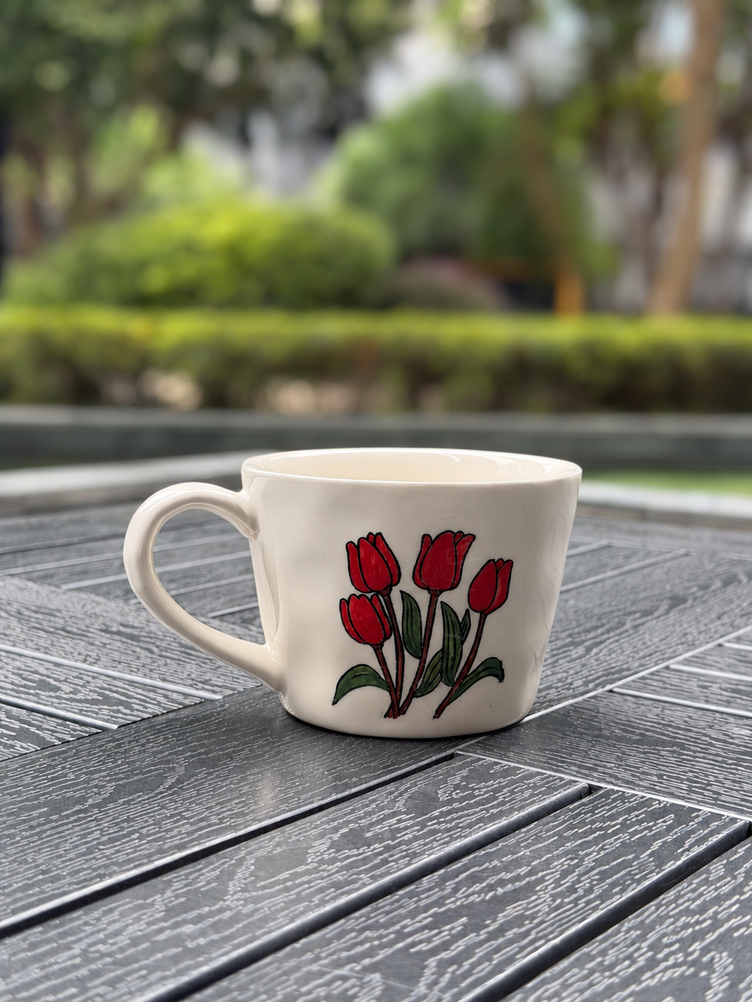 Reverse view of a cream ceramic mug featuring four hand-painted red tulips and green leaves