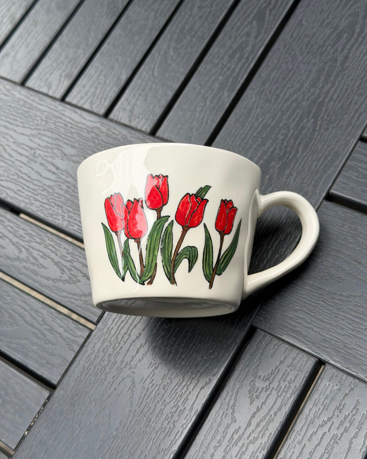 Hand-painted red tulip coffee mug lying on its side to show the full floral artwork and rounded shape