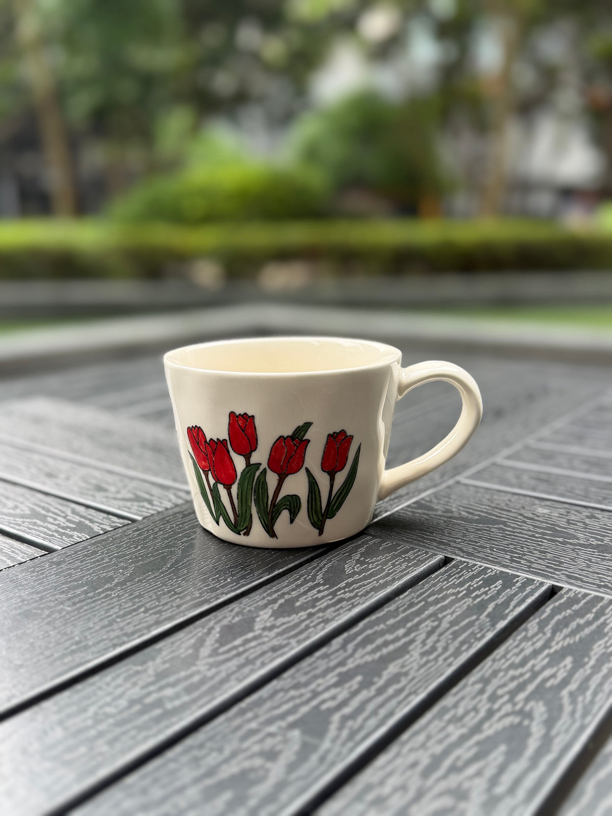 Side-angle view of a low rounded cream ceramic mug with a hand-painted red tulip garden design