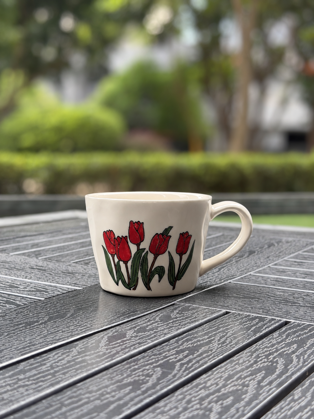 Front view of a 350 ml hand-painted red tulip coffee mug on an outdoor garden table