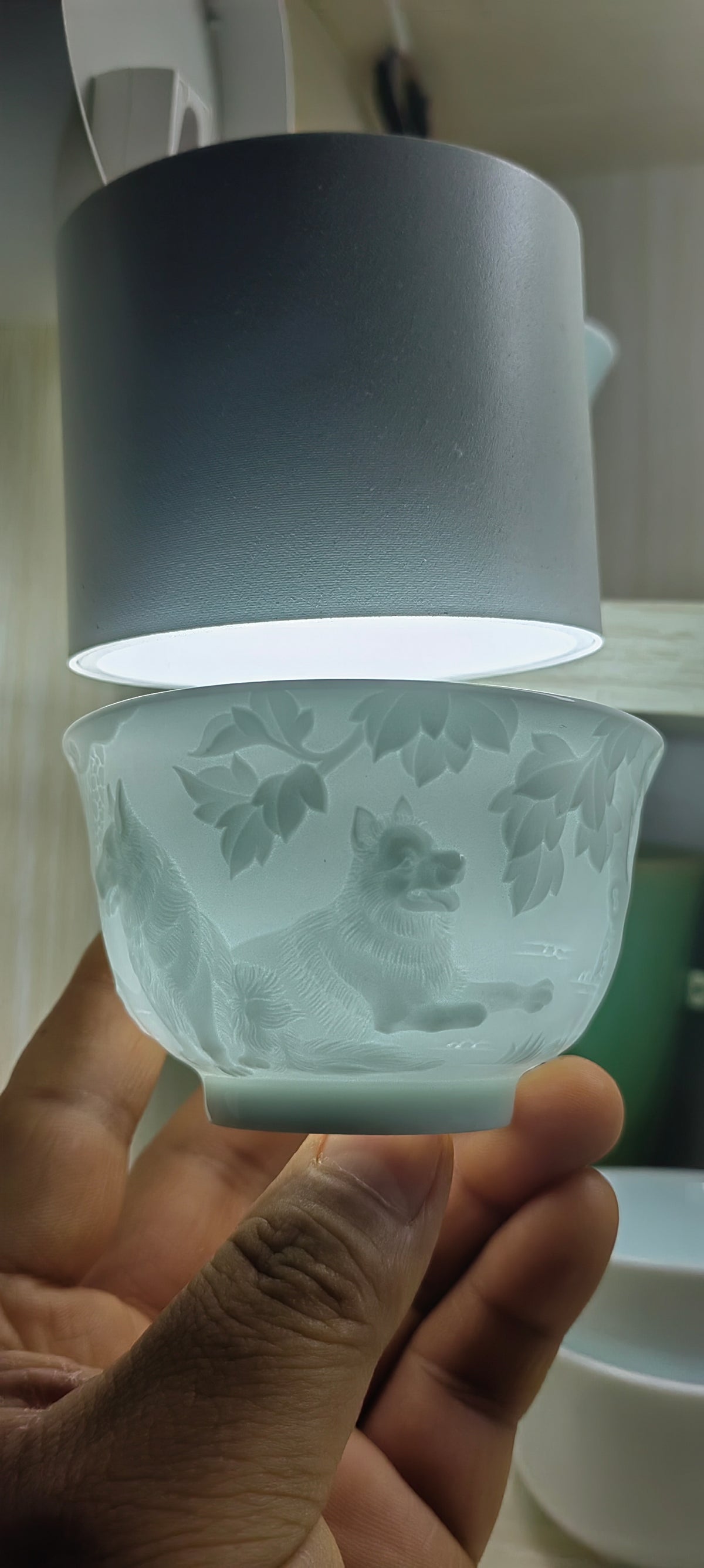 Hand-carved Dog Chinese Zodiac porcelain tea cup by Yan Wenlu shown under light to reveal the relief carving