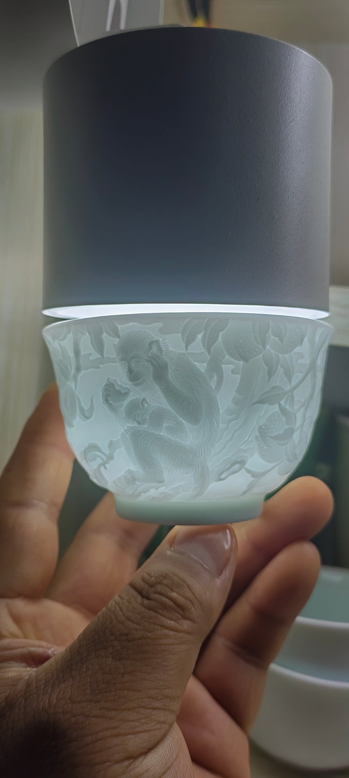 Hand-carved Monkey Chinese Zodiac porcelain tea cup by Yan Wenlu illuminated to reveal the fine relief details