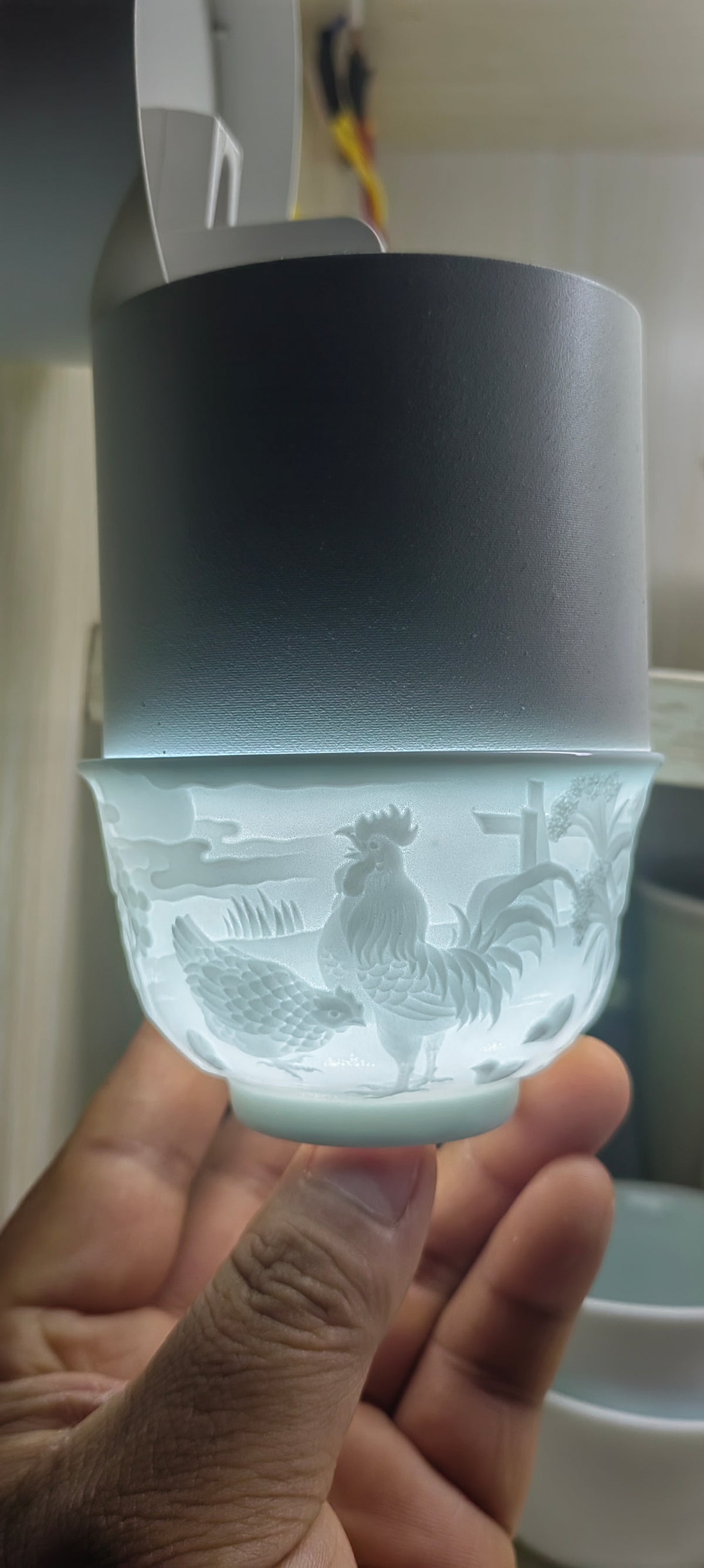 Hand-carved Rooster Chinese Zodiac porcelain tea cup by Yan Wenlu shown under light to reveal the detailed carving