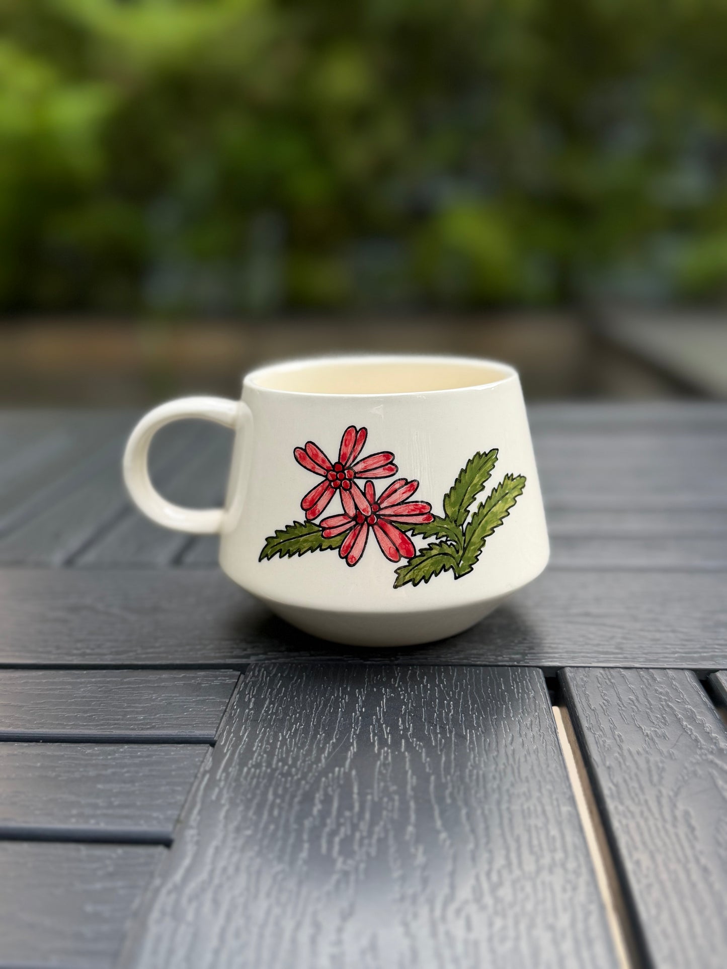 Back of Meadow Cow mug showing hand-painted floral design, photographed outdoors