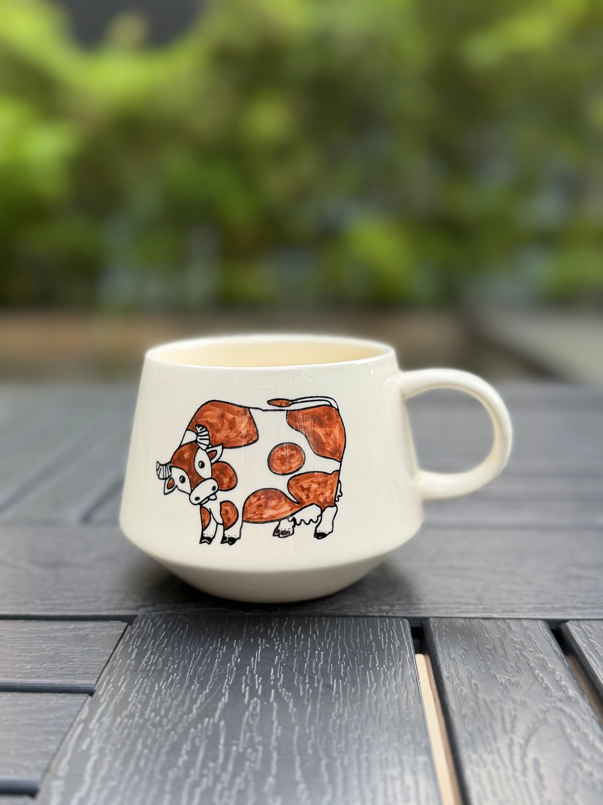 Meadow Cow ceramic mug with cow illustration photographed outdoors in natural light