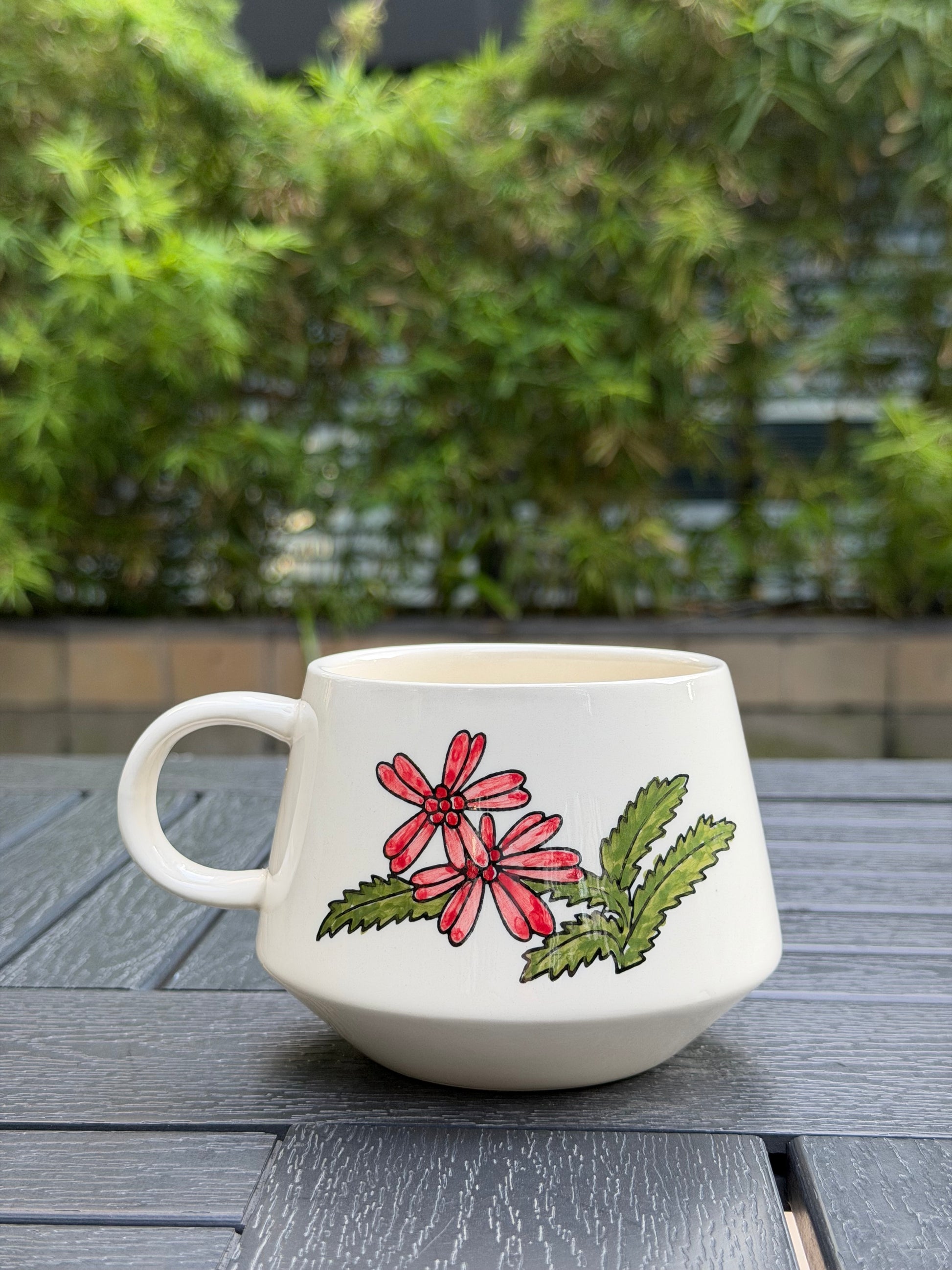 Back view of Meadow Cow ceramic mug featuring hand-painted red flowers and green leaves on cream glaze