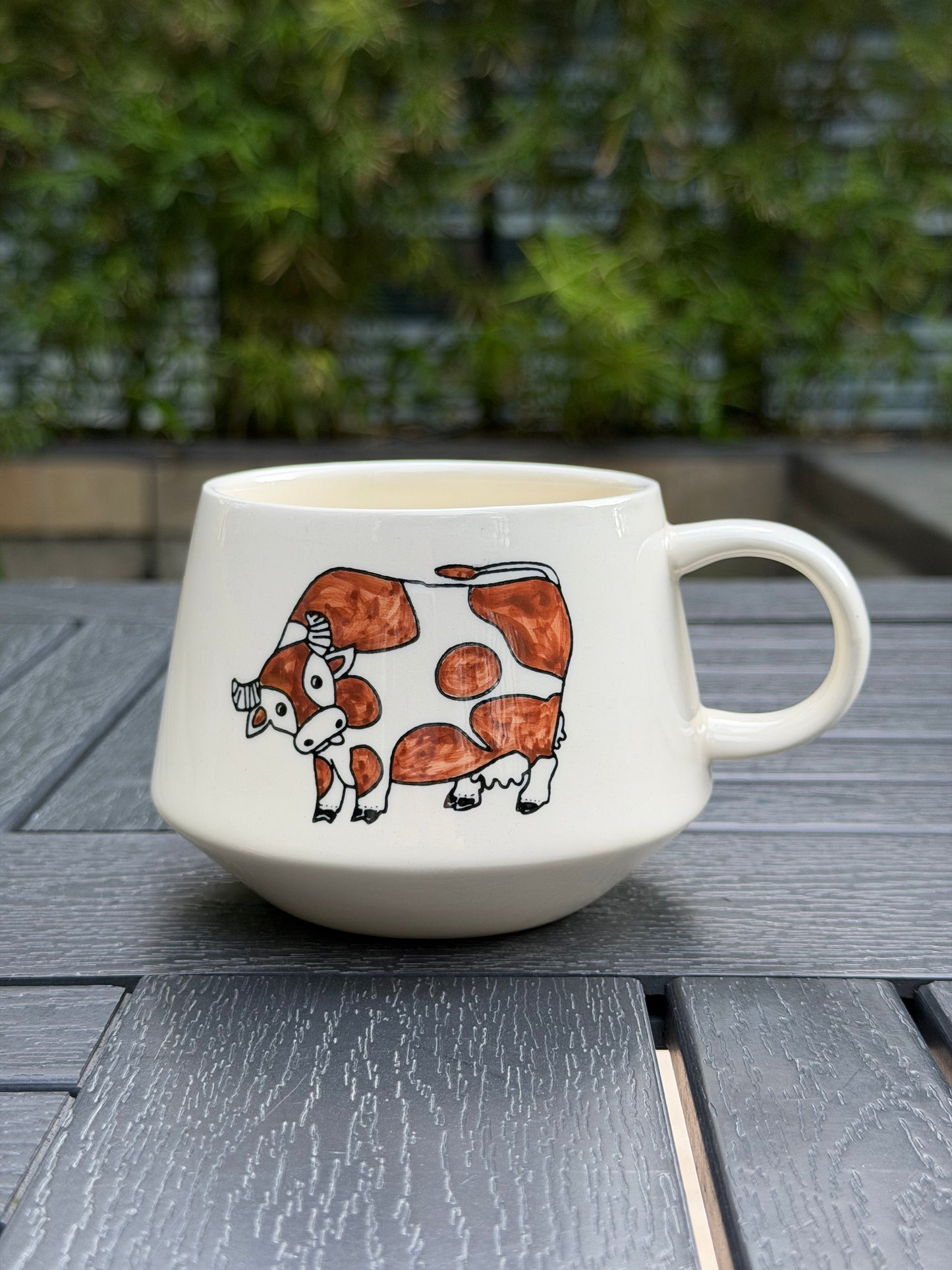 Front view of Meadow Cow hand-painted ceramic mug showing cow motif on cream body