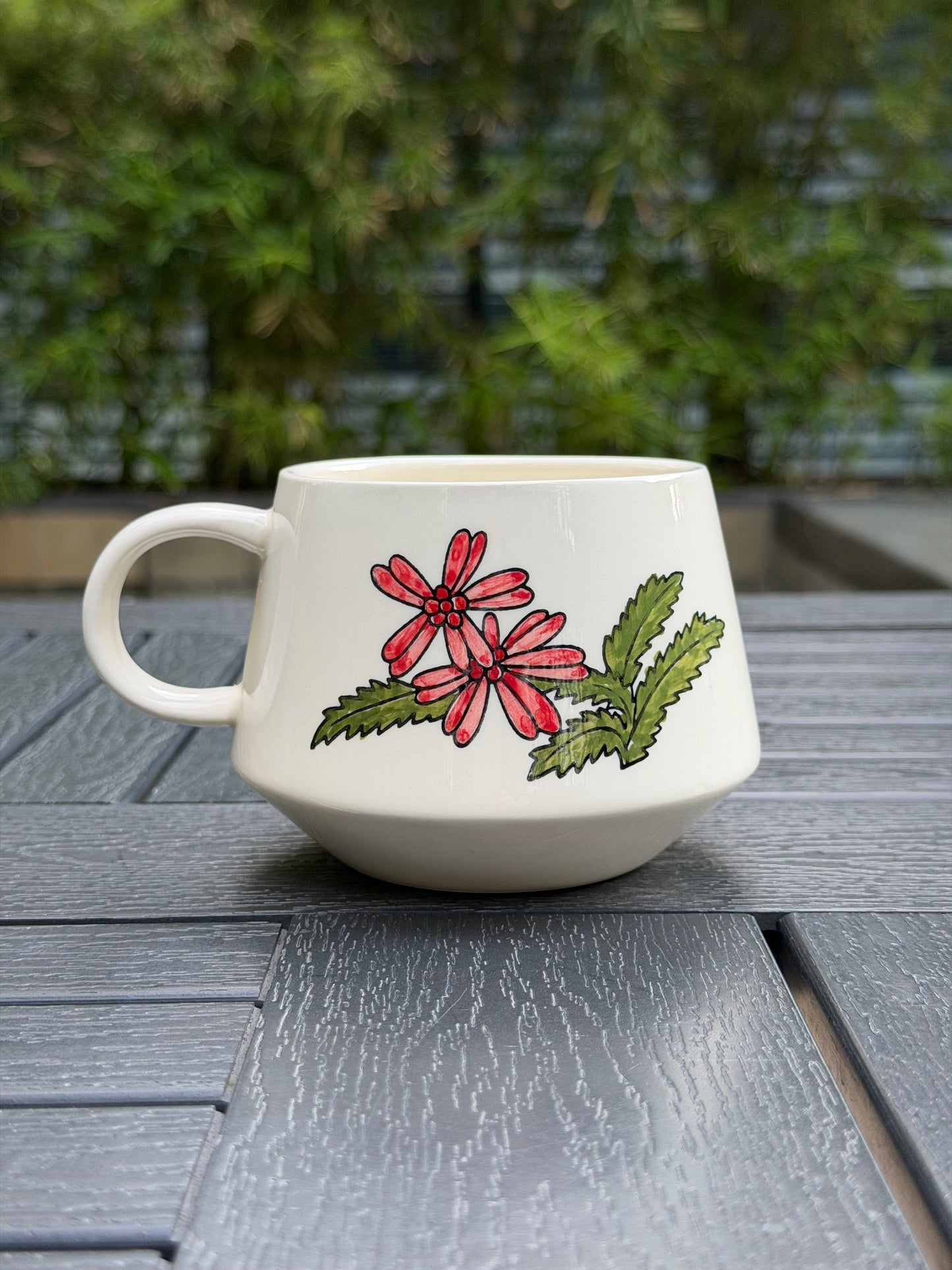 Close-up of hand-painted red flower and green leaf detail on the back of the Meadow Cow ceramic mug