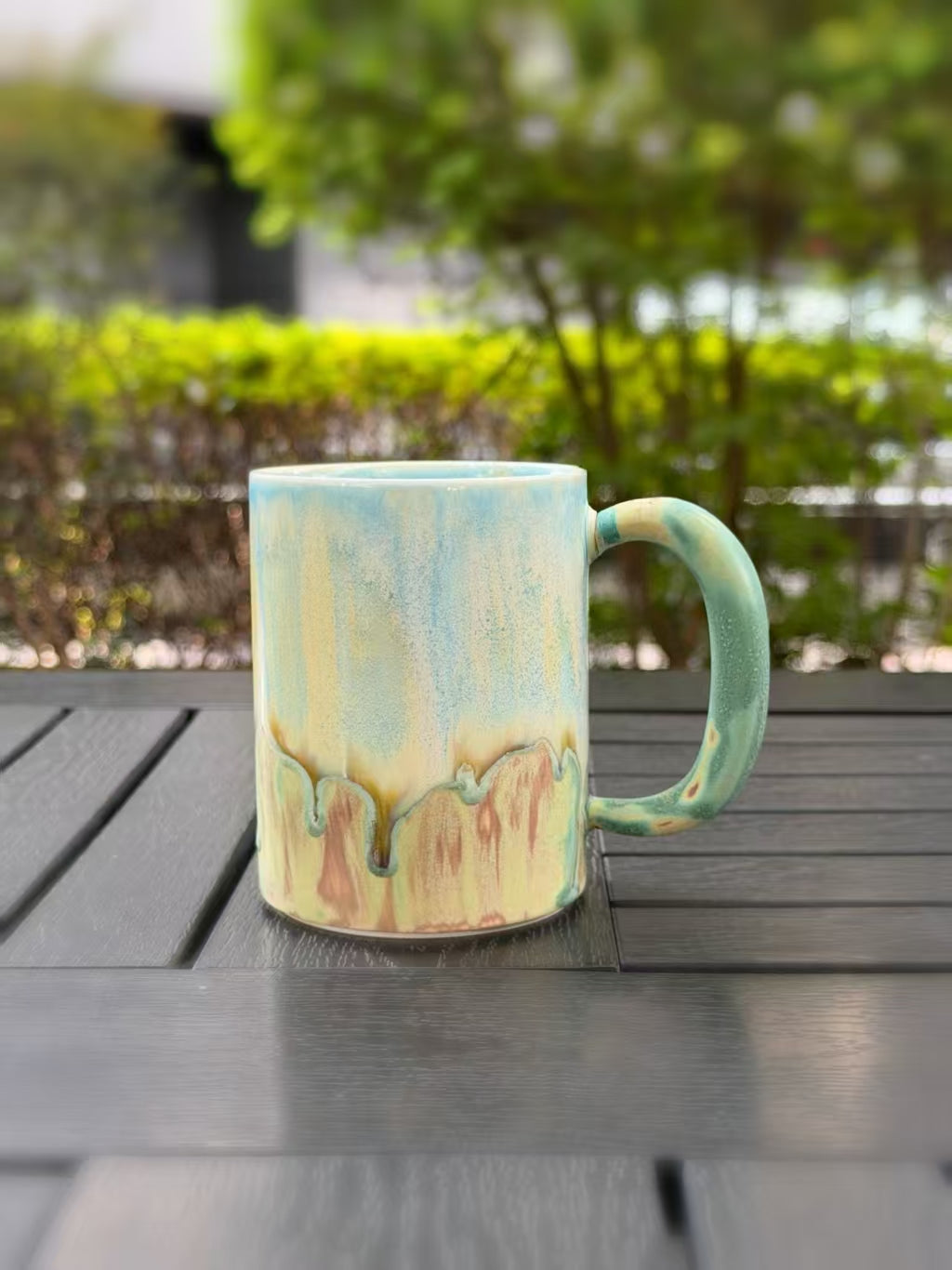 Handmade Jingdezhen mug with pale blue and yellow glaze flowing into green and warm earth tones, handle on the right.