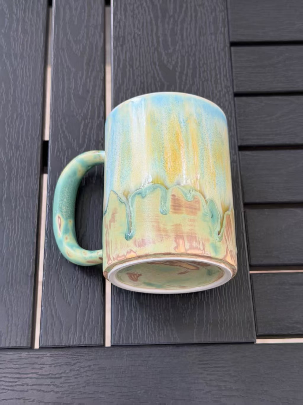Mug laid on its side to show the base, foot ring, green handle, and natural glaze variations.