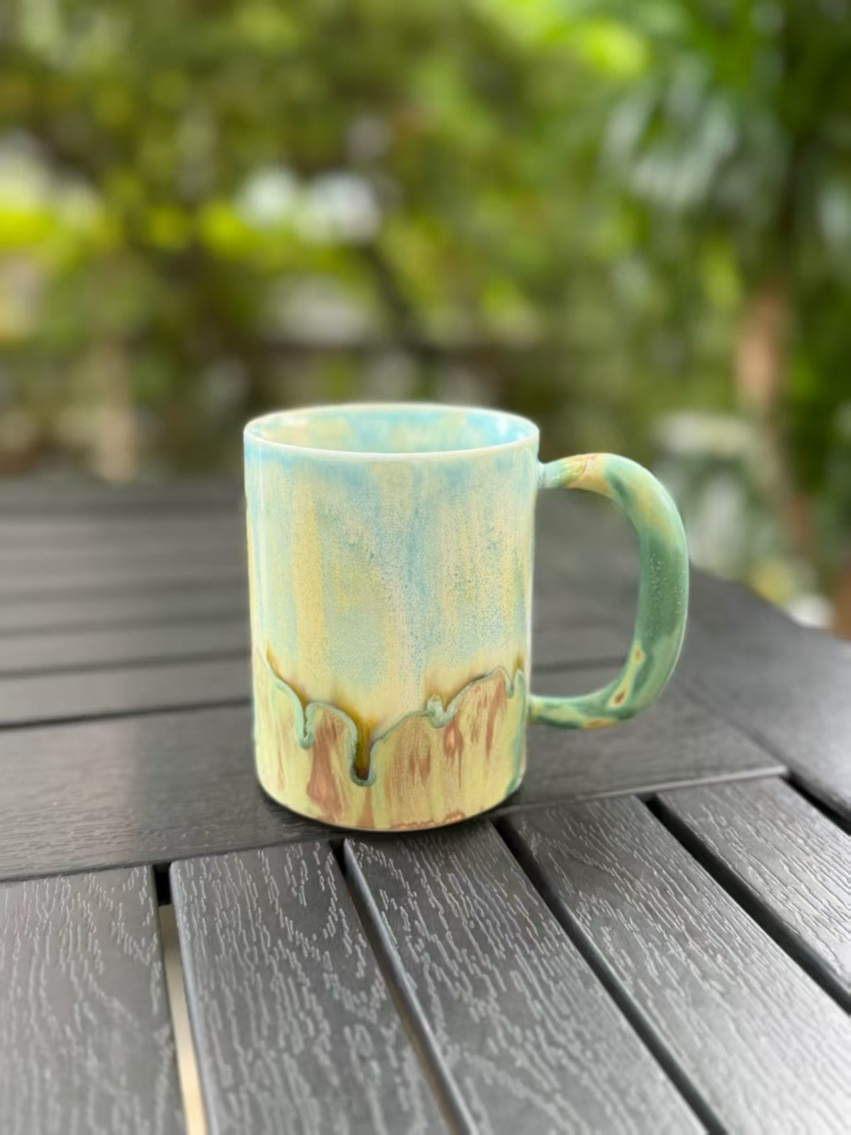 Angled front view of the kiln change mug showing its curved handle and softly blended blue, yellow, and green glaze.