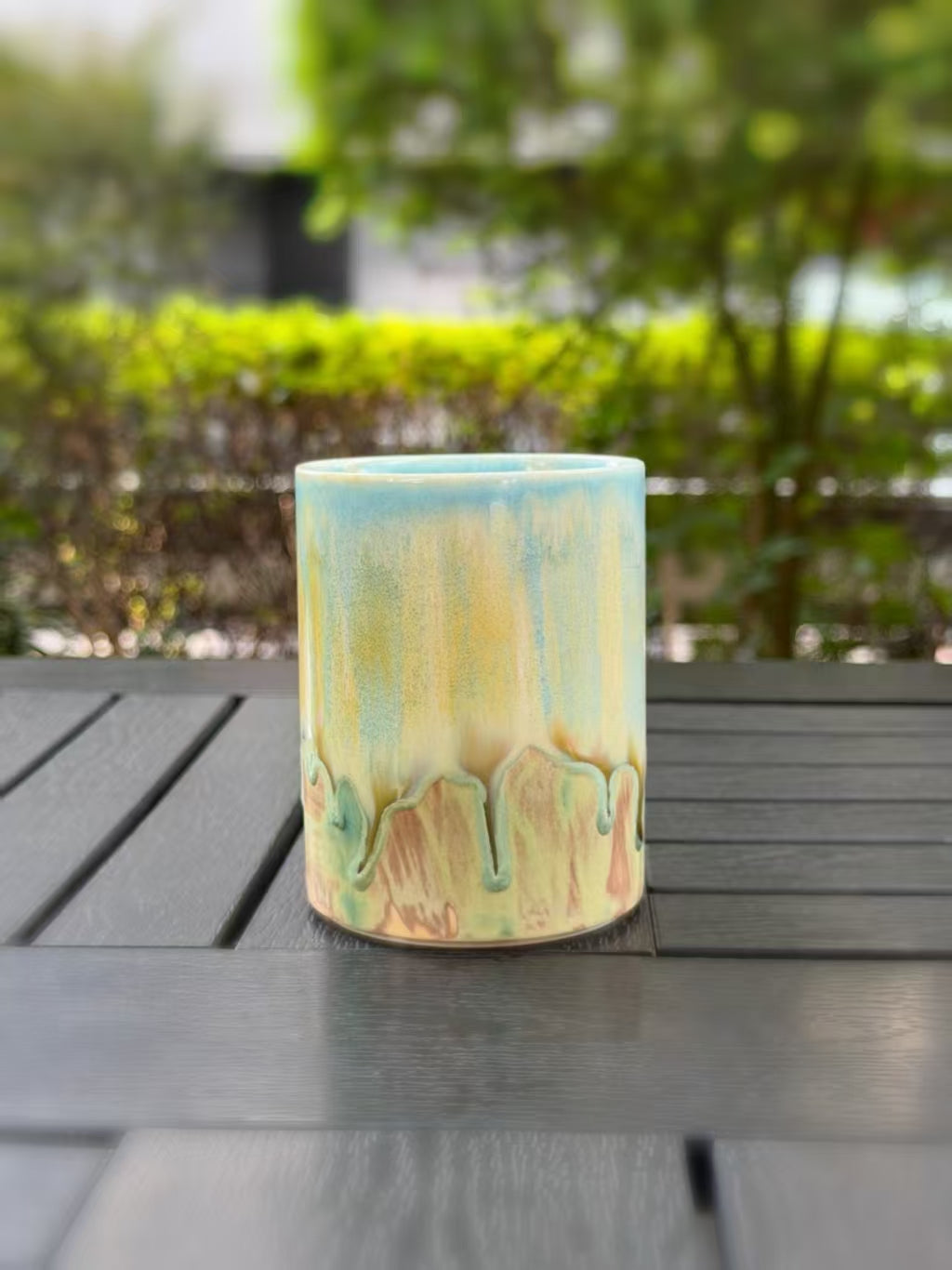 Side of the mug with the handle hidden, revealing uninterrupted blue and yellow glaze above irregular green drips.
