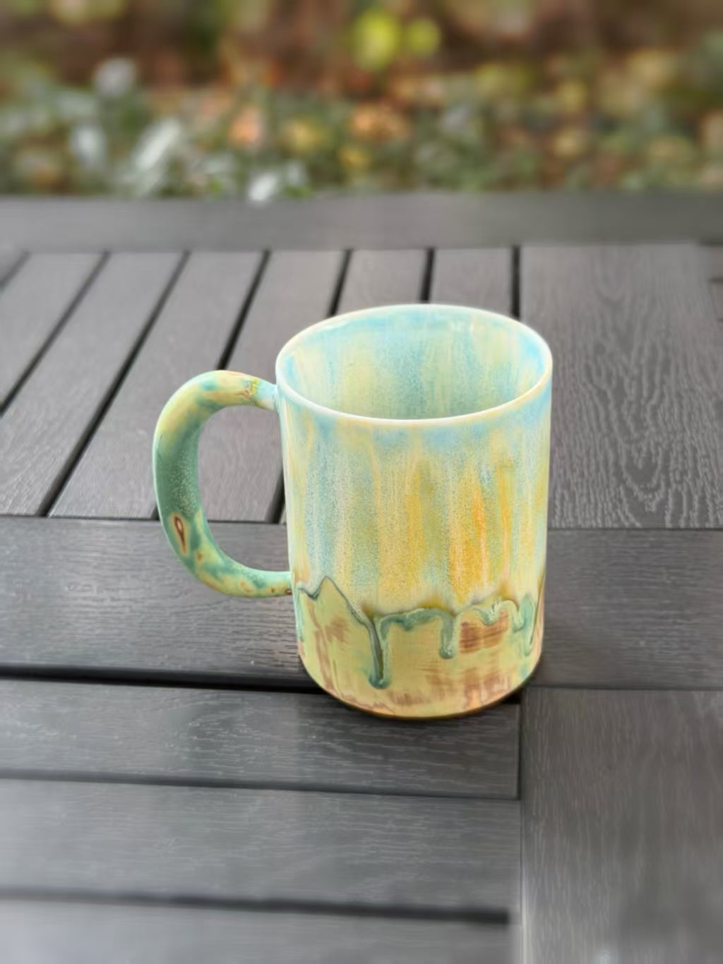 Slightly elevated view showing the mug’s pale blue interior, green handle, and flowing glaze across the outer wall.