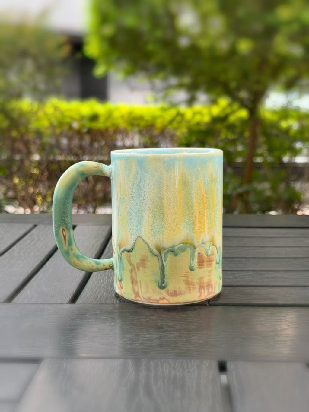 Reverse view of the handmade mug with the handle on the left and natural green glaze drips over warm earth tones.