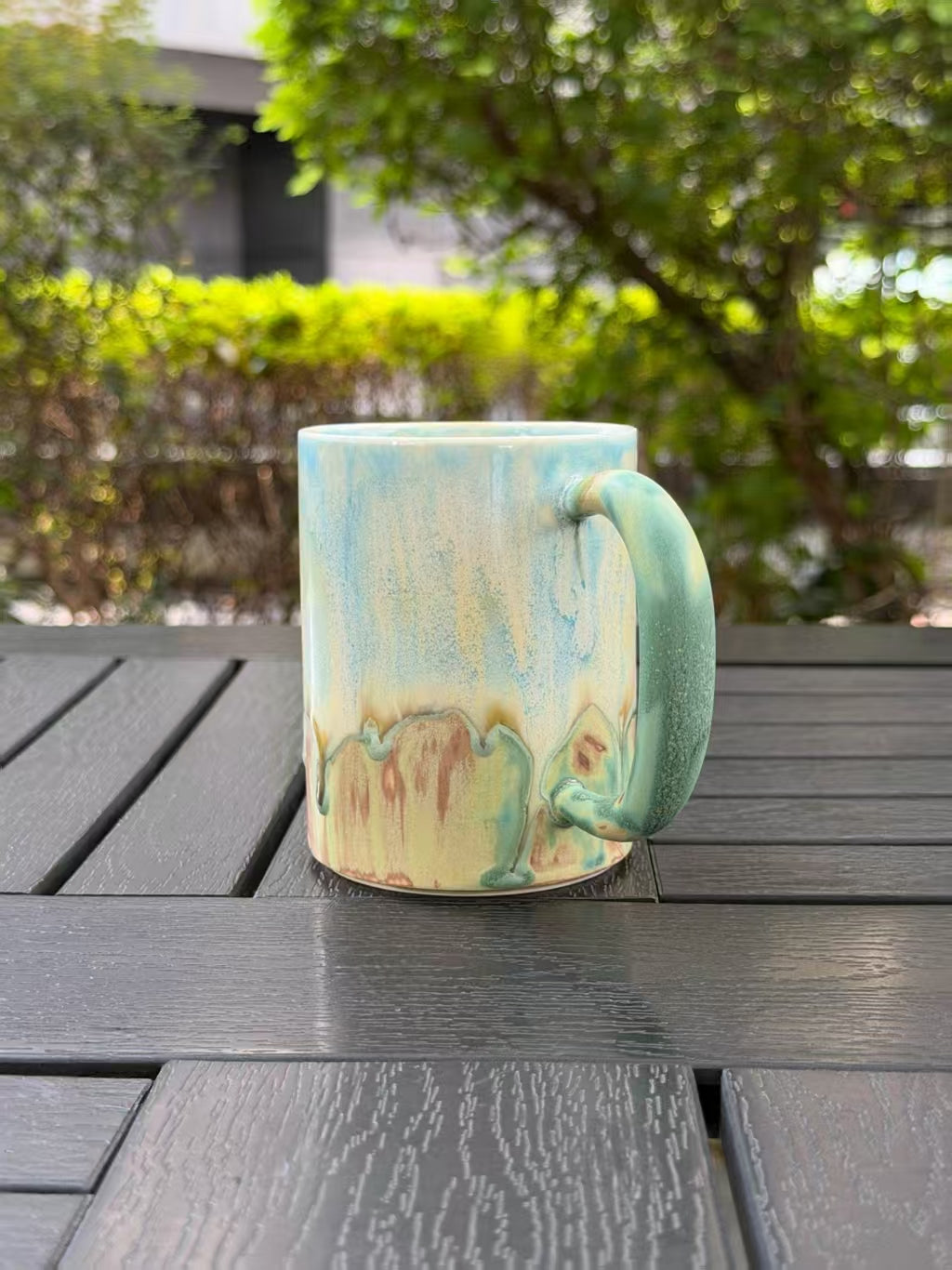 Opposite side view of the mug with the handle on the right and blue green glaze flowing into earthy tones.