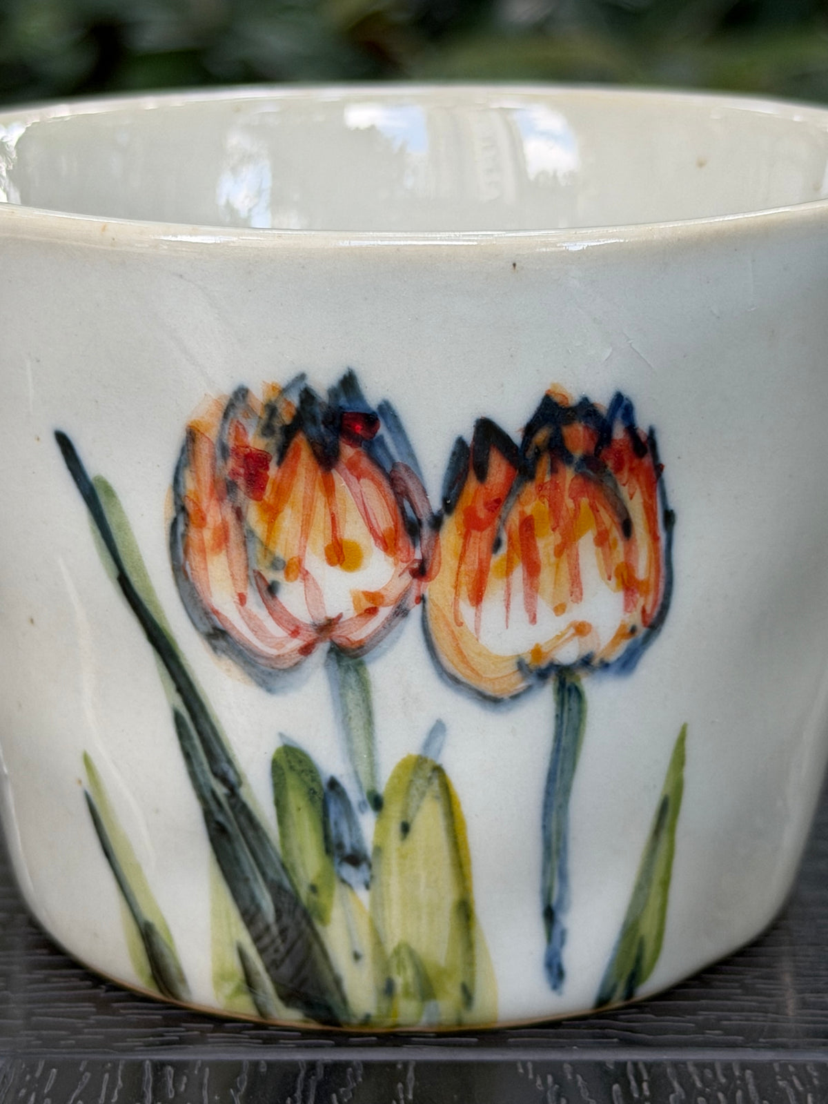 Close-up of freehand orange tulip brushwork on a high-fired stoneware mug