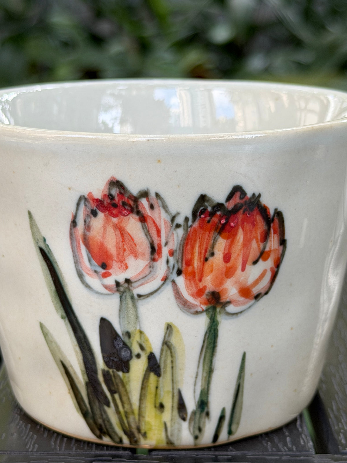 Close-up of individually hand-painted orange tulips and leaves on grey stoneware