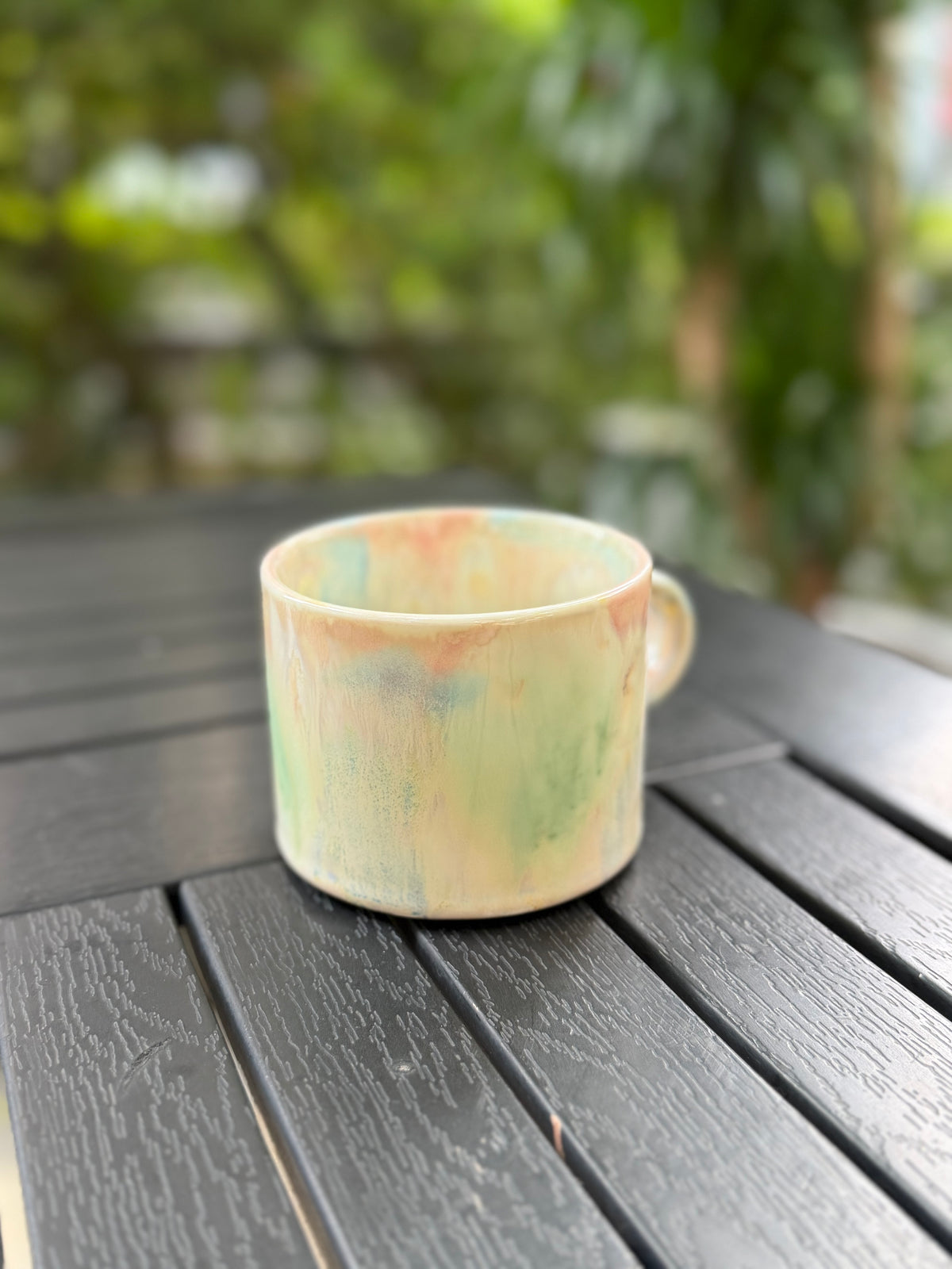 Pastel Meadow reactive glaze mug photographed outdoors with soft greenery in the background