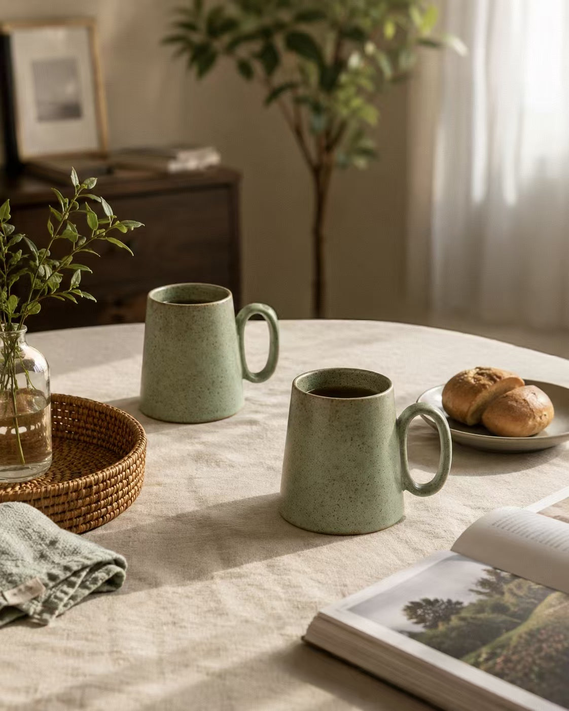 Two Quiet Meadow Mugs on a linen-covered dining table with bread rolls and greenery – slow morning at home
