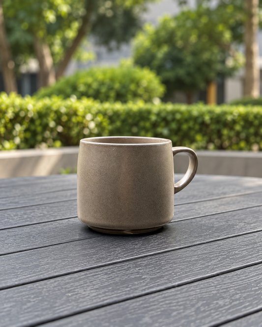 Warm Stone 440 ml ceramic mug with a subtly textured grey-brown glaze on an outdoor table in a softly blurred garden
