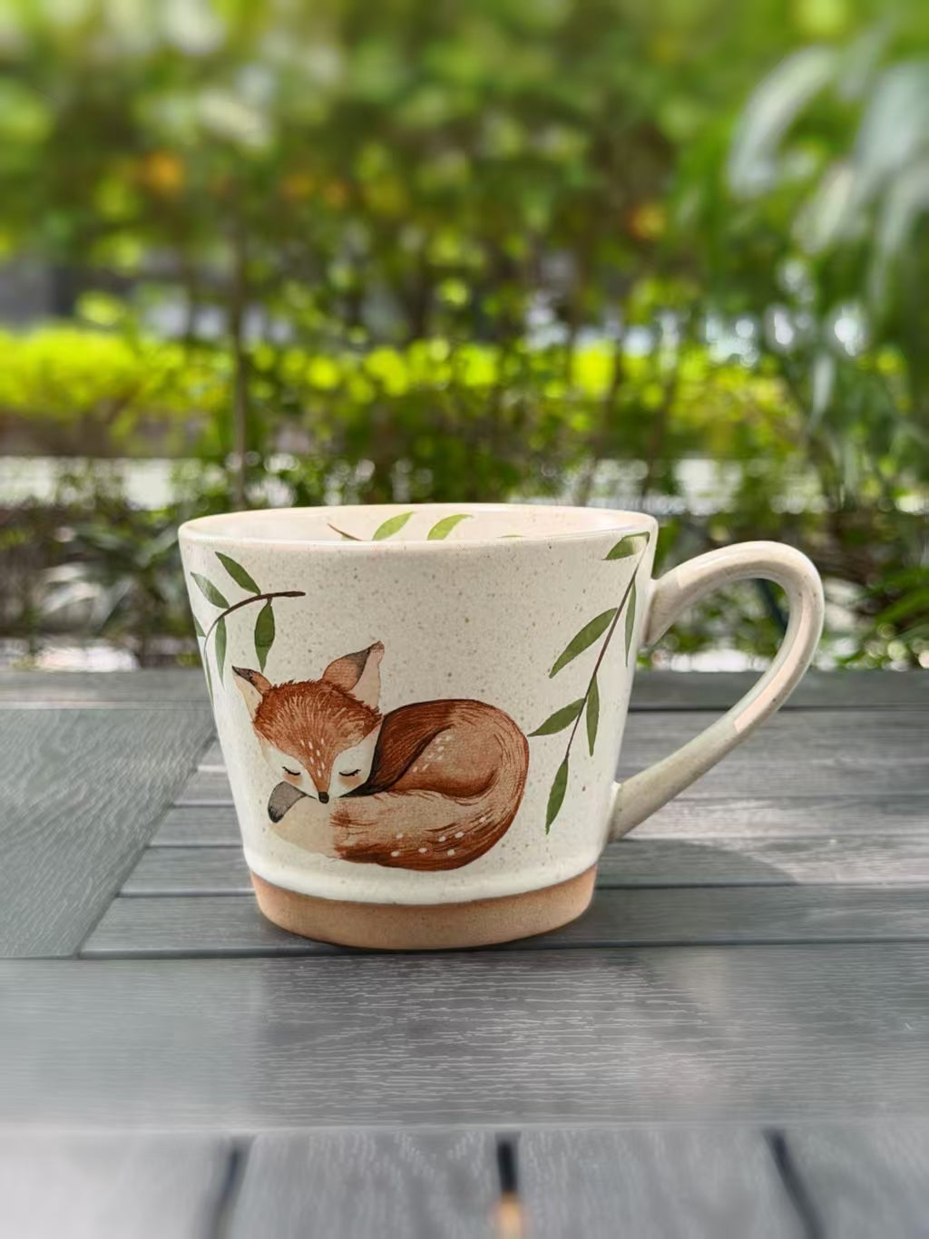 Cream ceramic mug with a sleeping fox beneath green branches and the handle on the right