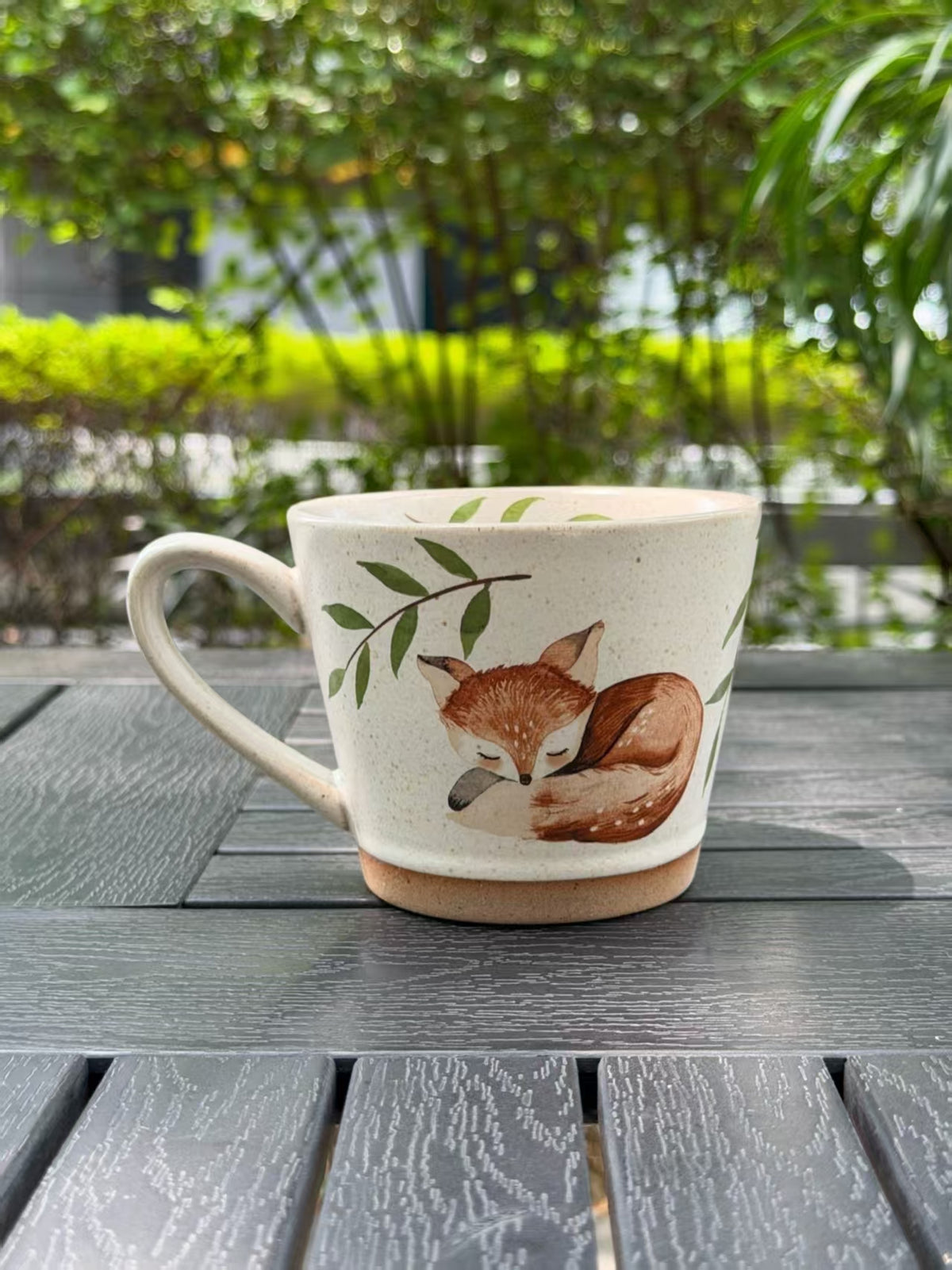 Reverse side of the ceramic mug showing a sleeping fox and leafy branches, with the handle on the left