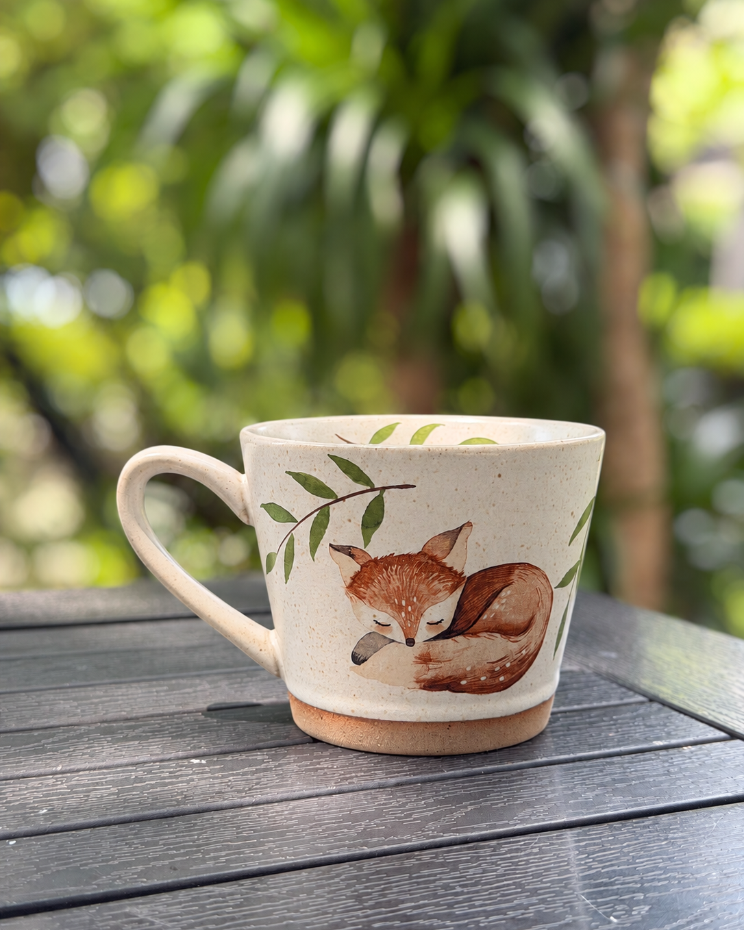 Reverse view of the sleeping fox mug on an outdoor table, with its handle on the left
