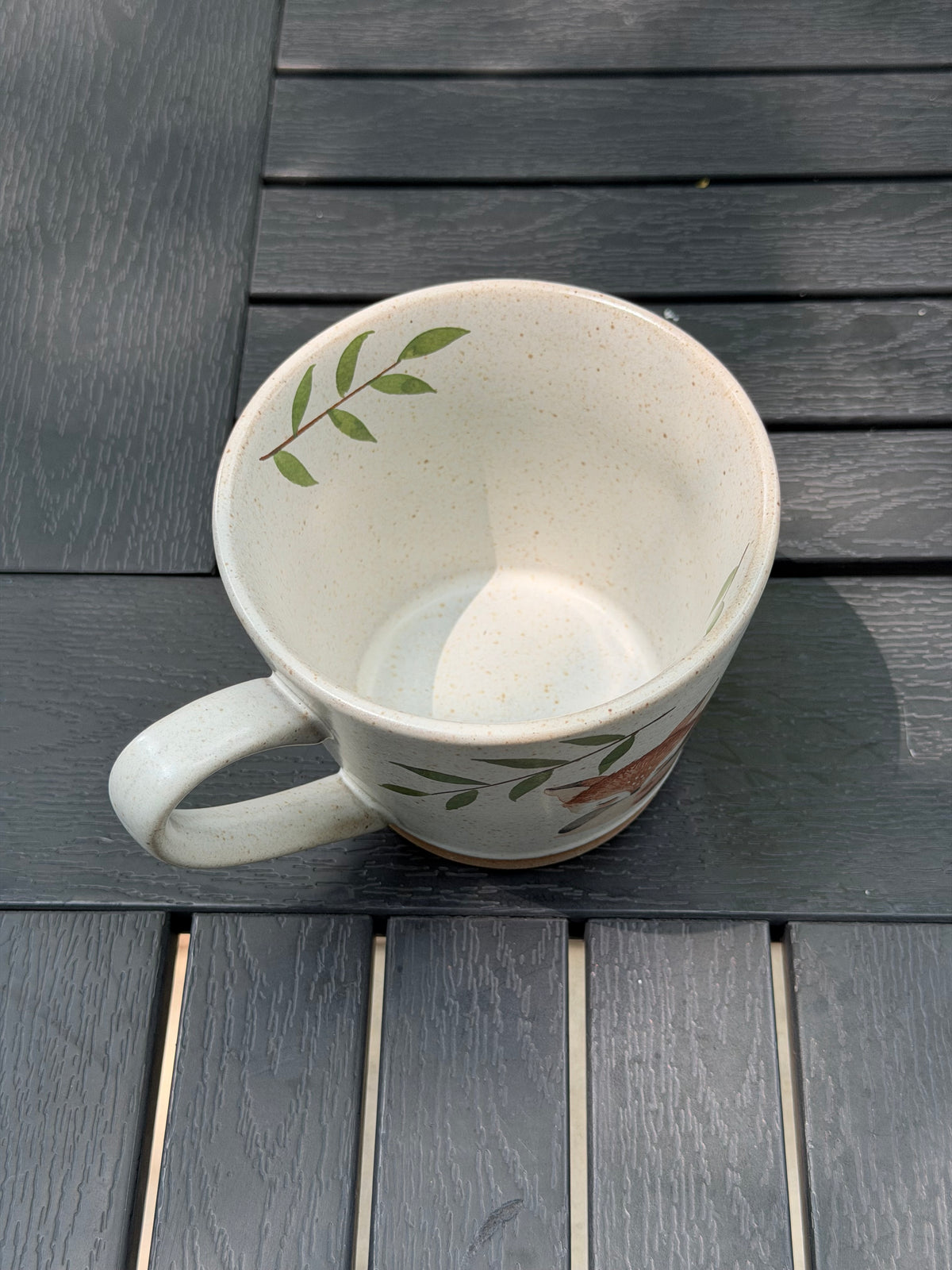 View into the cream ceramic mug showing the leafy branch near the inner rim and the bottom of the cup