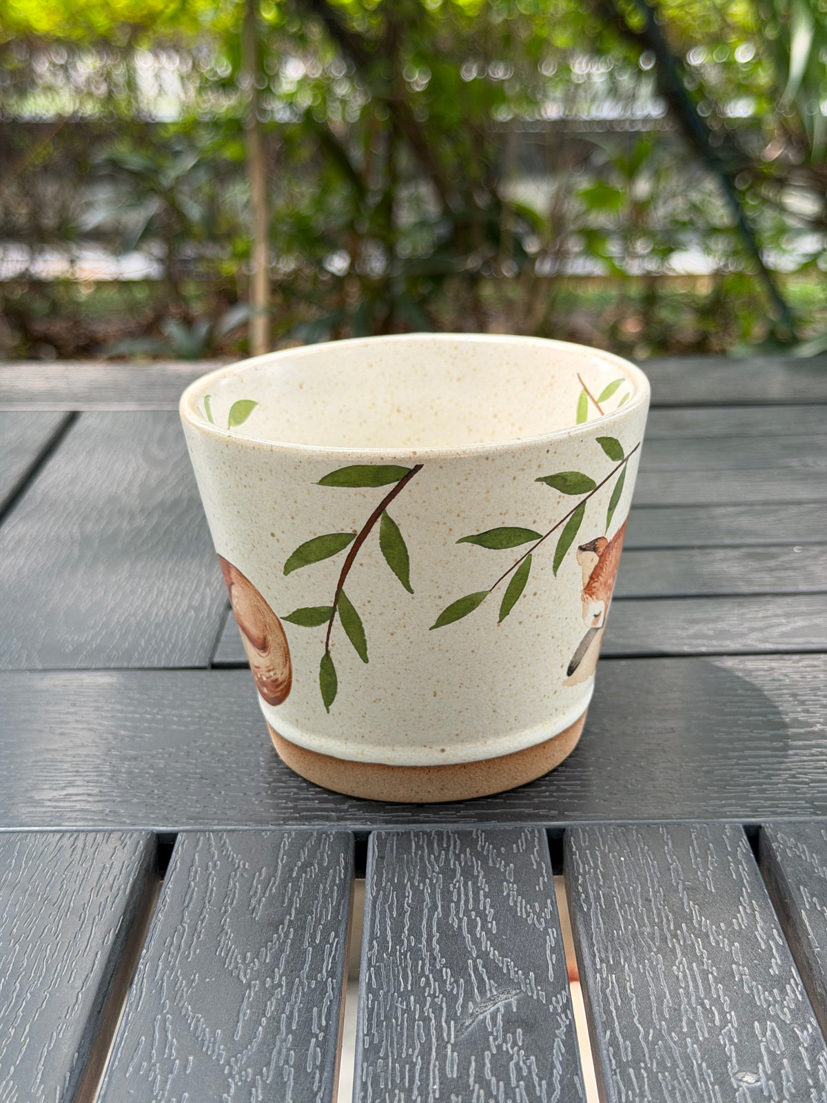 Side of the cream mug showing green branches between the fox illustrations
