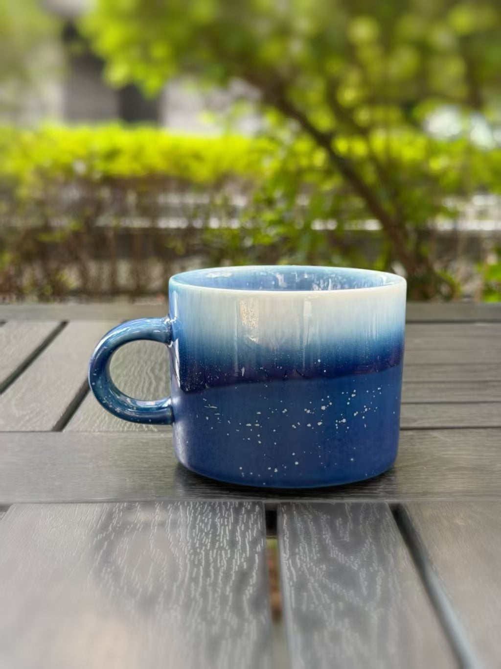 Closer back view of the ceramic mug showing the flowing blue glaze and fine pale specks
