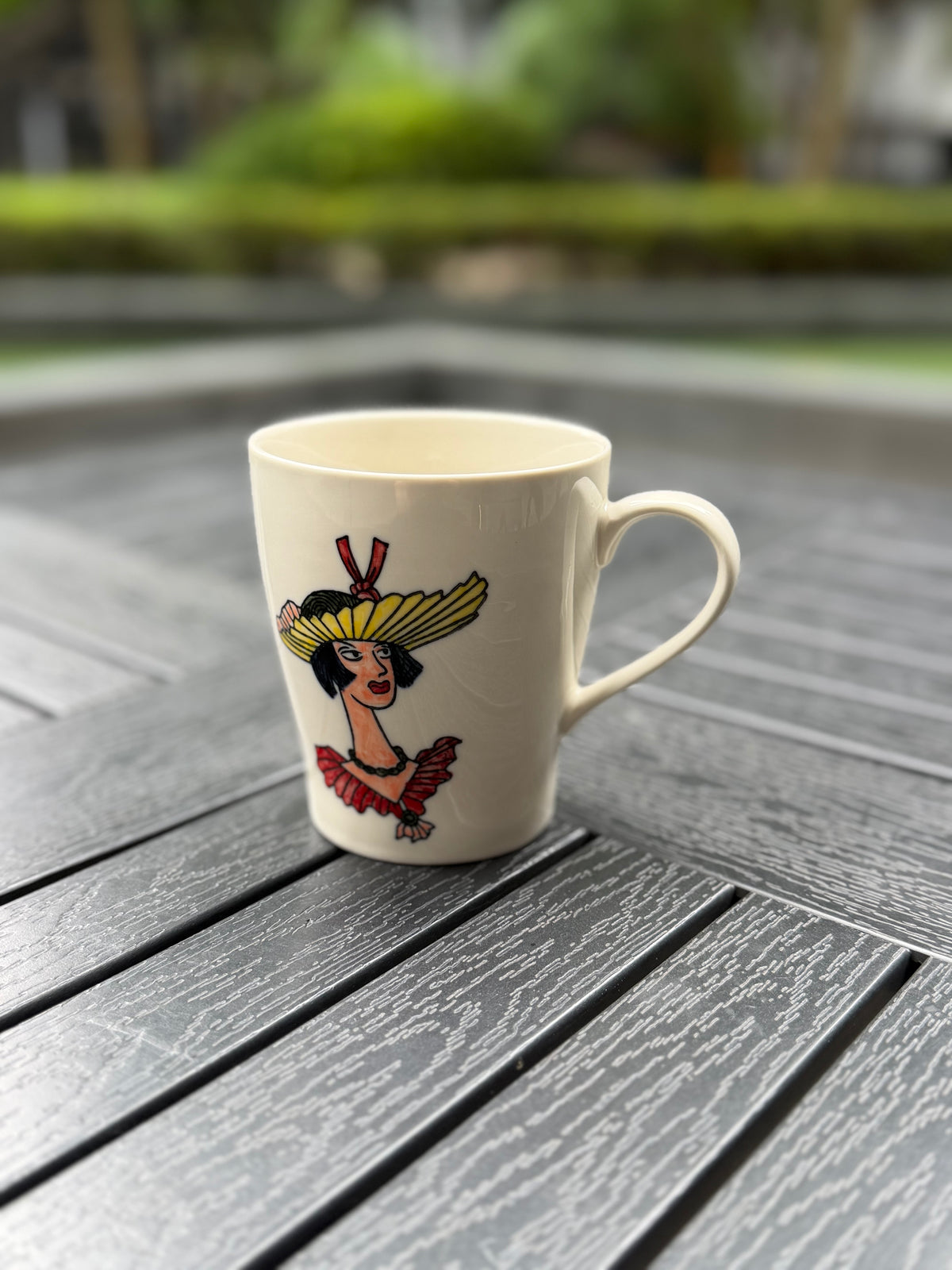 Angled view of the Sunflower Muse hand-painted ceramic mug featuring a woman in a yellow sunflower hat on an ivory glaze.