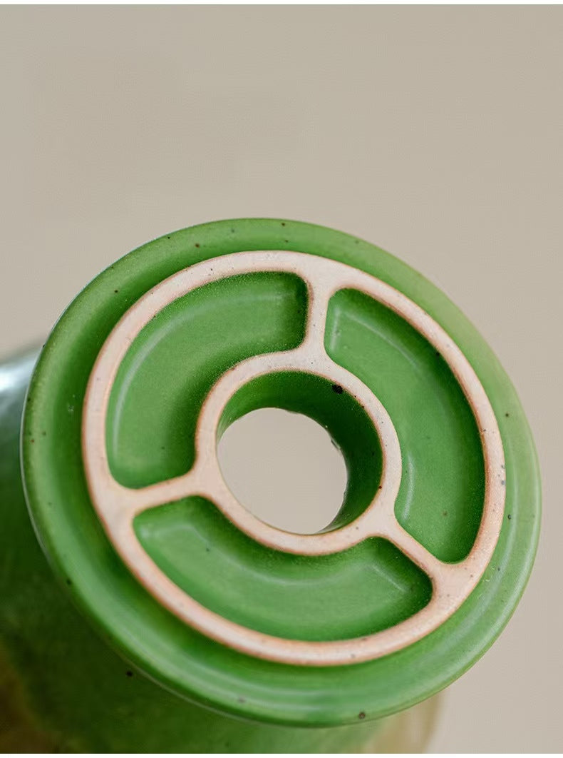 Close-up of the bottom of a green ceramic bottle or vessel, showing a circular base with a beige ring and segmented circular design around a central hole.