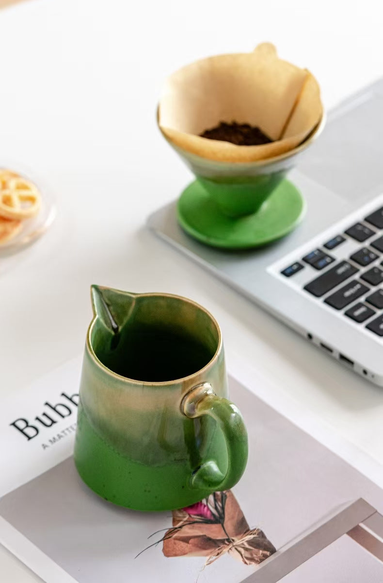 Green ceramic pour-over coffee set on a desk workspace beside a laptop