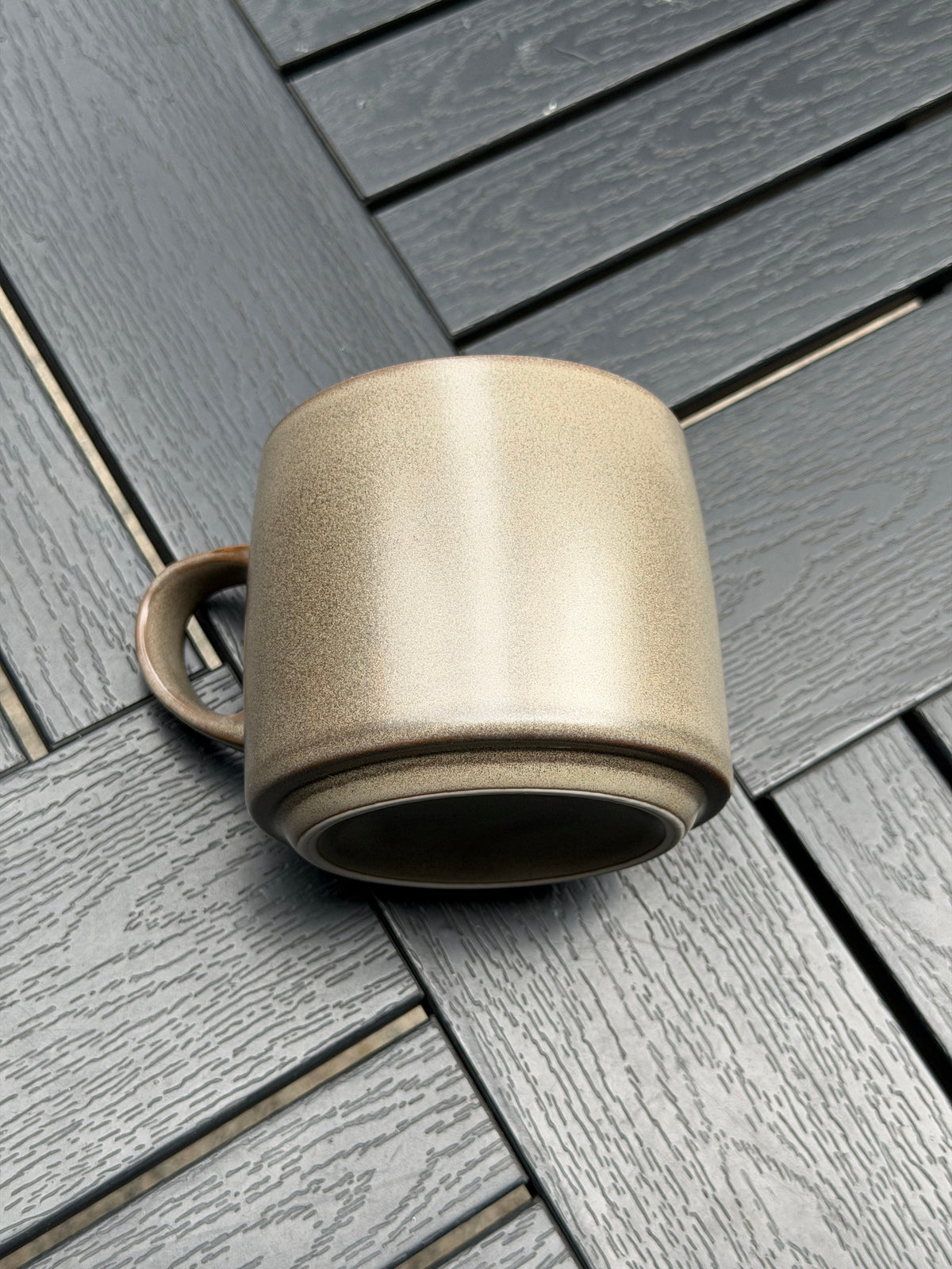 Warm Stone ceramic mug resting on its side to show the base, textured grey glaze and curved handle