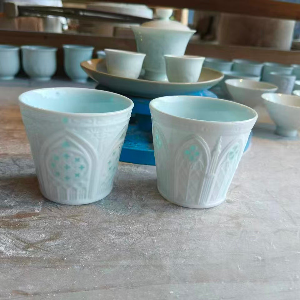 Two hand-carved Linglong porcelain cups with pale celadon accents displayed in the artist’s studio